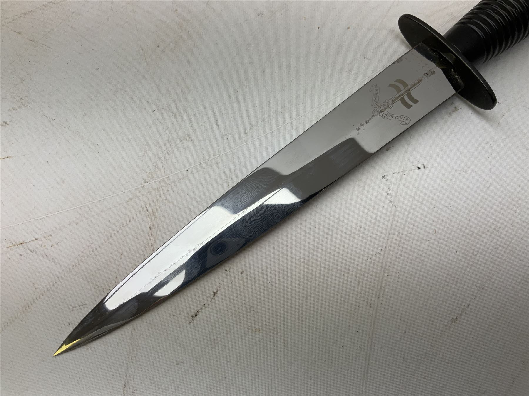 Gulf War period commando knife with 17cm double-edged steel blade etched with the crest and motto 'By Strength and Guile', blackened cross-piece and grip; in webbing scabbard L31cm overall