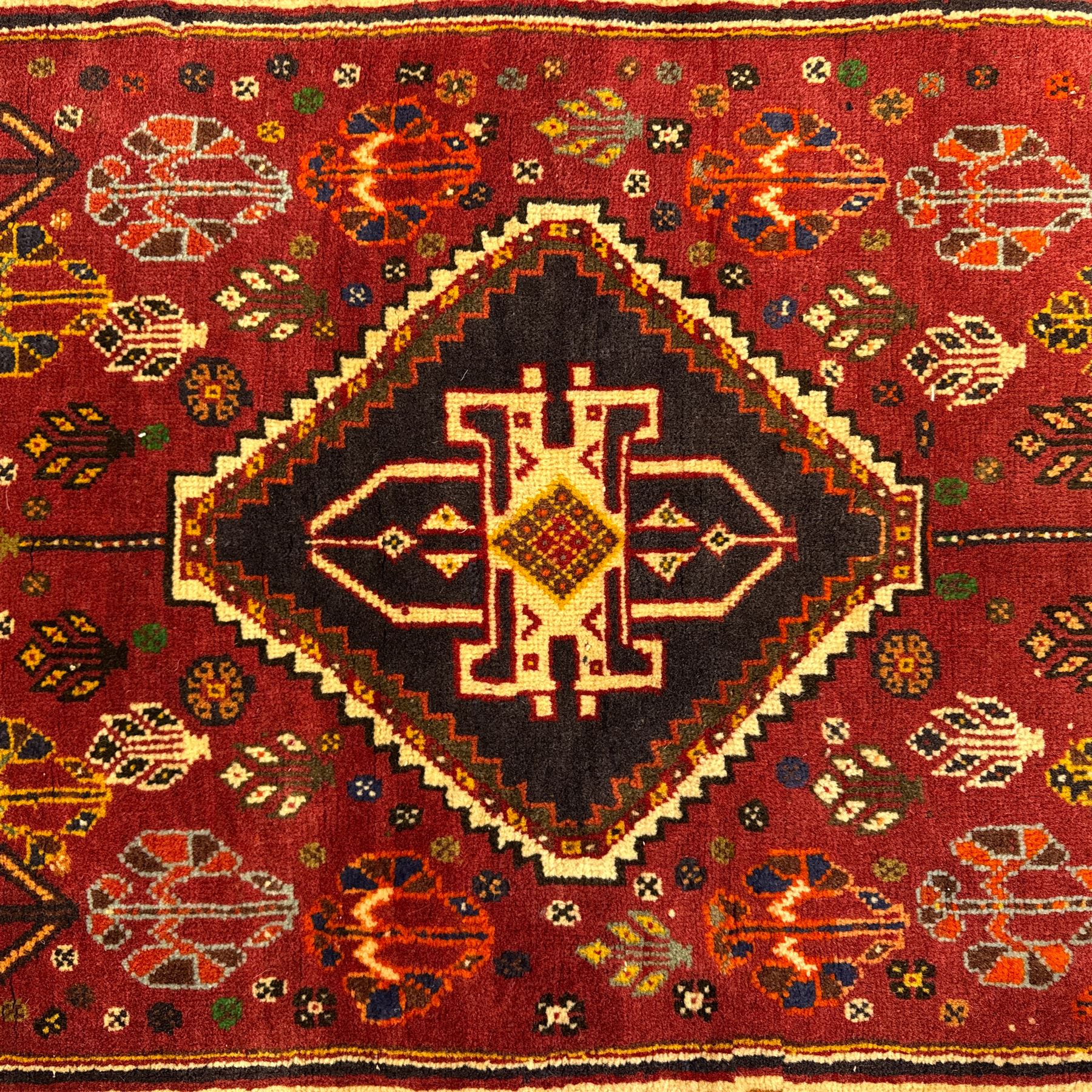 South West Persian Qashqai rug, hand knotted wool with central dark blue lozenge medallion containing geometric motifs, on a madder red field decorated with stylised floral boteh motifs, indigo spandrels, multiple borders of floral rosettes, from the region of Fars, south-west Persia