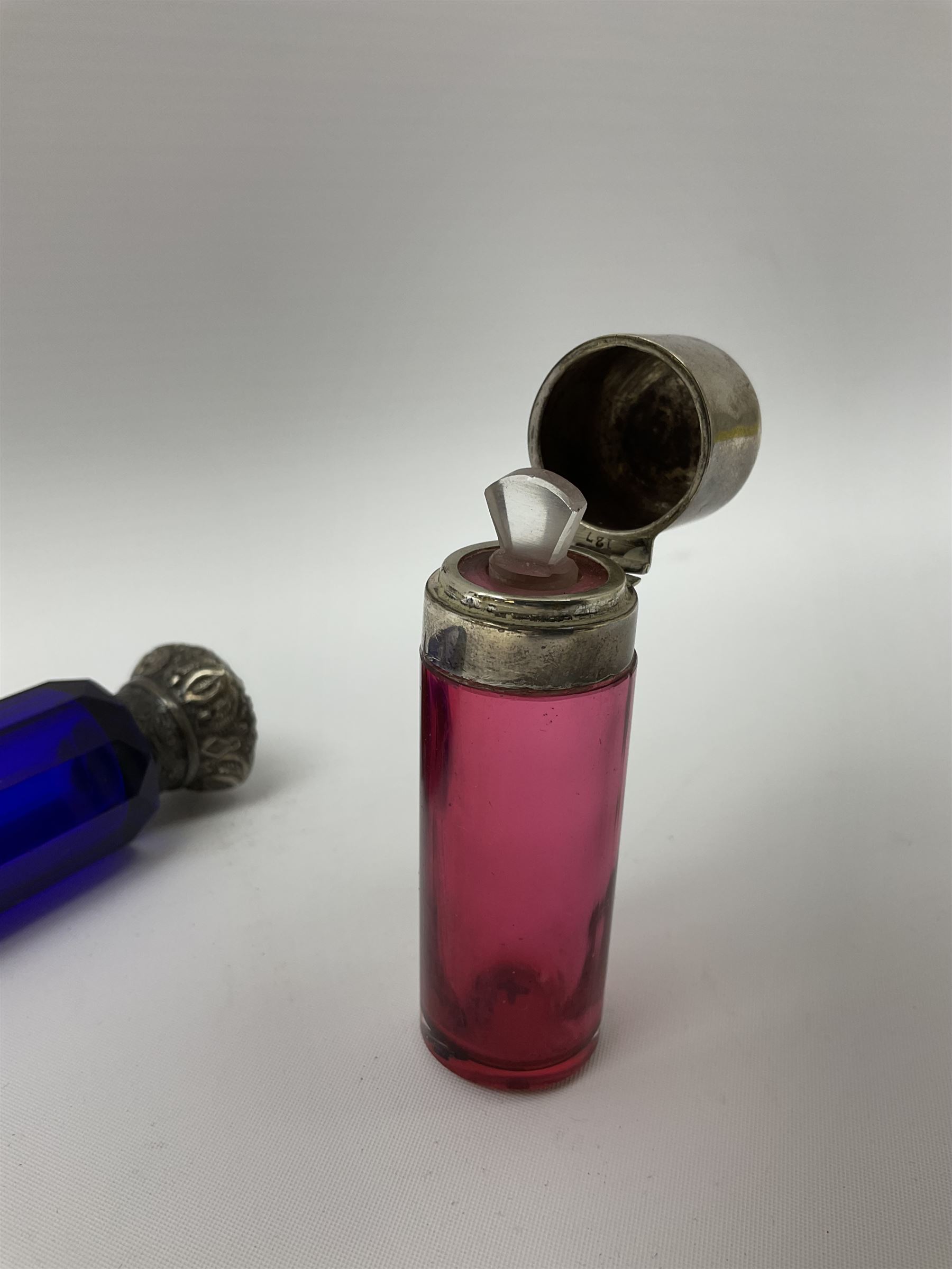 Late Victorian silver mounted ruby glass cylindrical scent bottle, with interior glass stopper, Birmingham 1900, makers mark worn, H8cm, together with a Victorian double ended cut blue glass perfume bottle mounted with white metal screw and flip caps decorated with foliate repousse detailing, H13.5cm