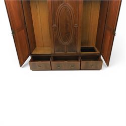 Edwardian inlaid mahogany triple wardrobe, featuring two oval mirror doors with bevelled plates, enclosing central figured veneered panel with mouled detail, above three base drawers