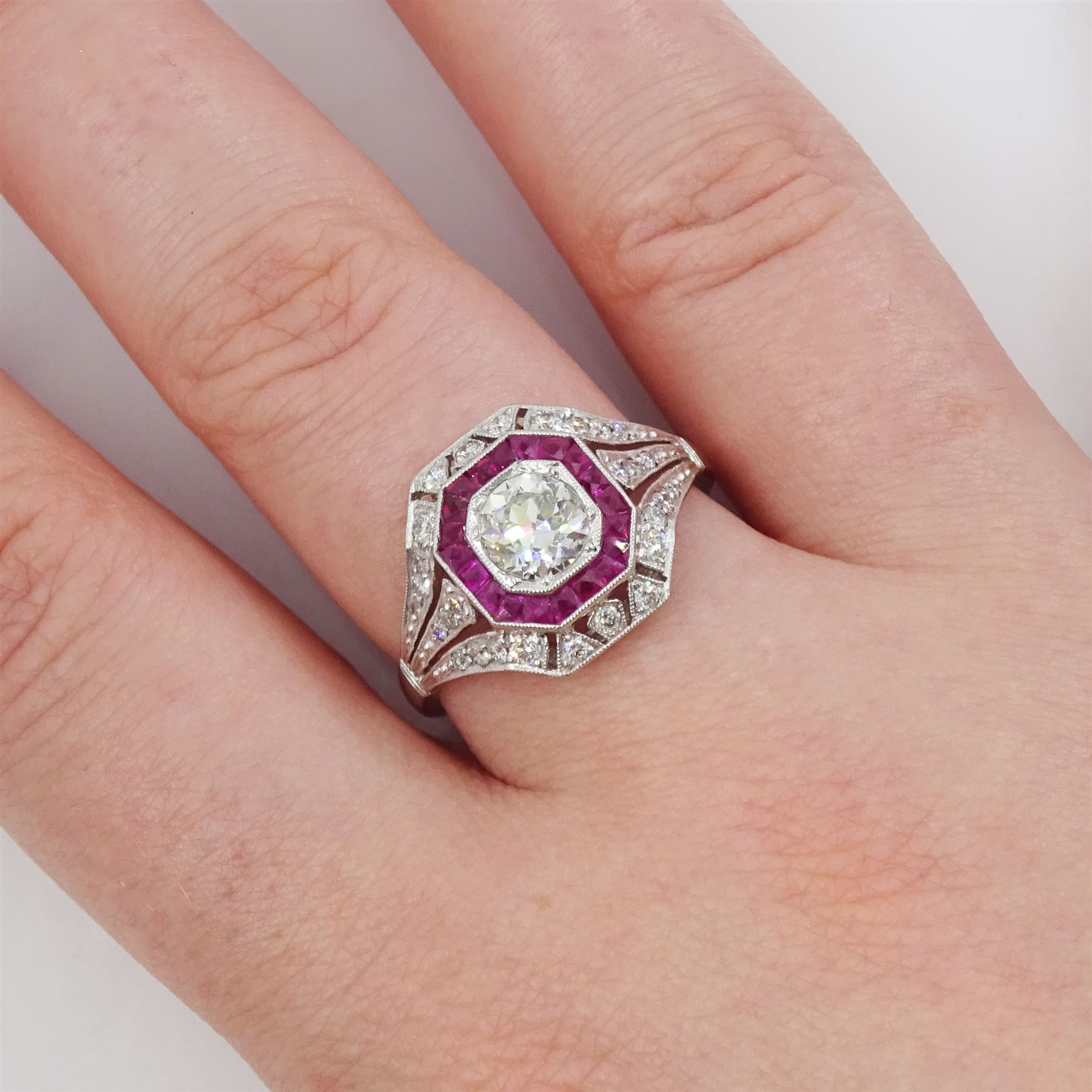 Platinum diamond and ruby cluster ring, the principal transitional cut diamond of approx 0.65 carat, in an octagonal milgrain setting, surrounded by calibre cut rubies, to further round brilliant cut diamonds and a split design shoulders