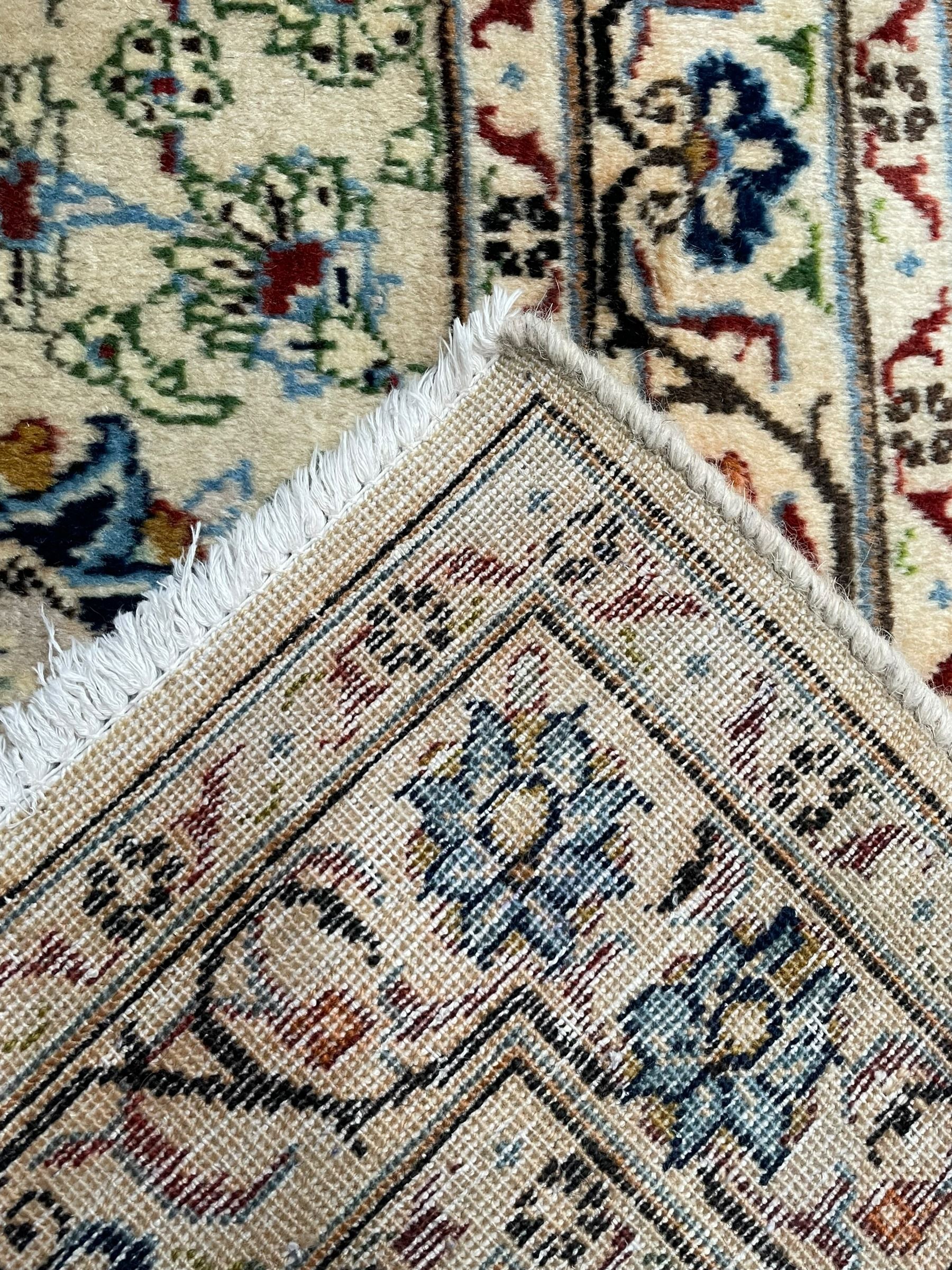 Persian Kashan ivory ground carpet, the field decorated with swirling foliate patterns and stylised plant motifs, scrolling border decorated with palmettes, within floral pattern guard stripes 