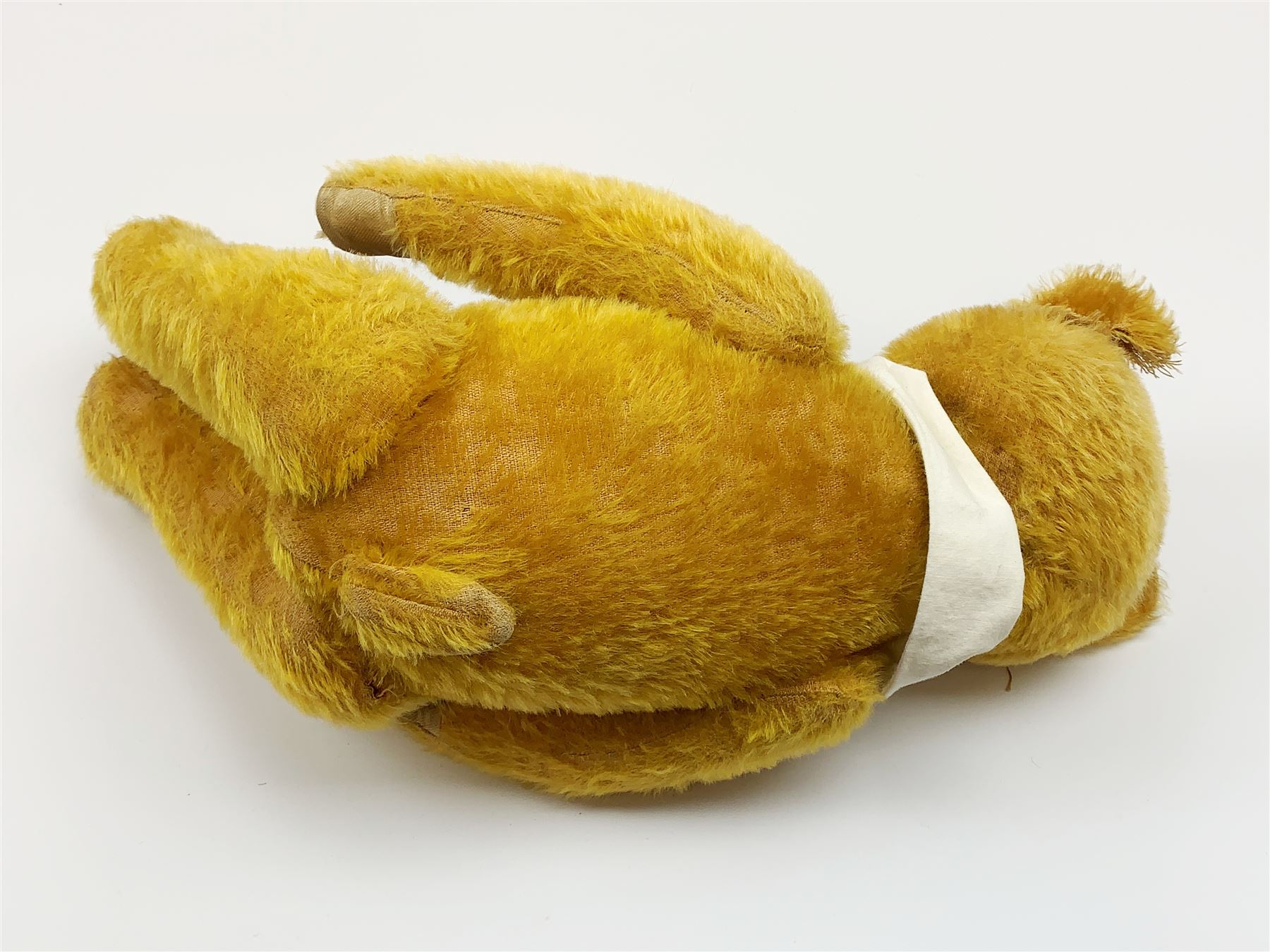 Schuco 'yes-no' teddy bear c1925 with wood wool filled short golden mohair body, linen pads with stitched claws and  tail-operated moving head with glass eyes and vertically stitched nose and mouth H18