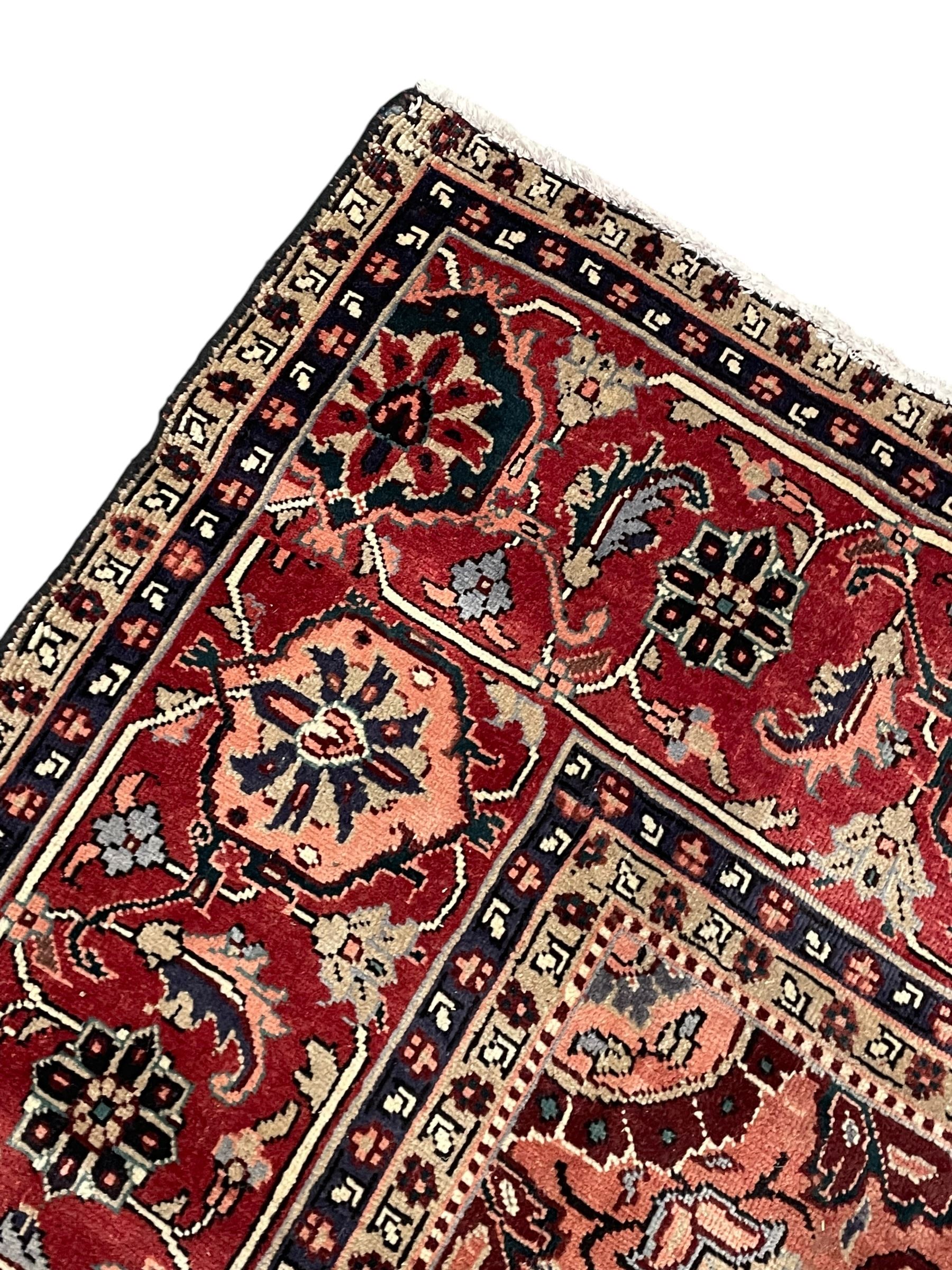Persian Heriz dark indigo and red ground carpet, the central medallion with large projecting palmette motifs, overall floral design decorated with stylised plant motifs, repeating patterned border within guard stripes