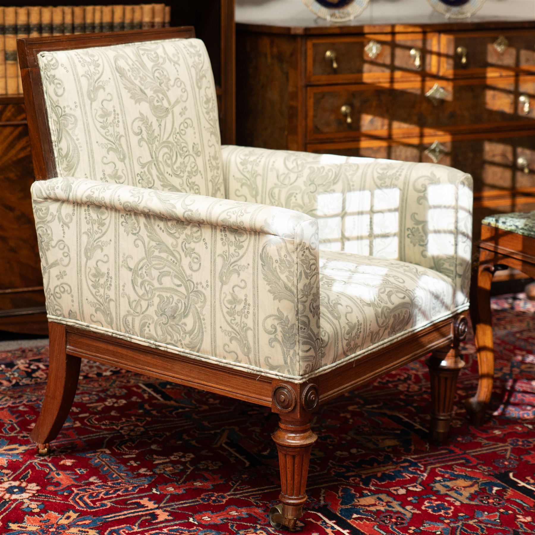 William IV rosewood framed library armchair, squared form with green on ivory ground upholstery, moulded lower seat rail with applied roundels over reeded supports, terminating to brass cups and castors