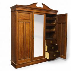 Edwardian walnut triple wardrobe, shaped broken-arch pediment over three doors comprising central mirrored door flanked by moulded raised and fielded panelled doors, interior fitted with hanging space and a bank of three open drawers above three brass recessed-pull drawers, on moulded plinth base