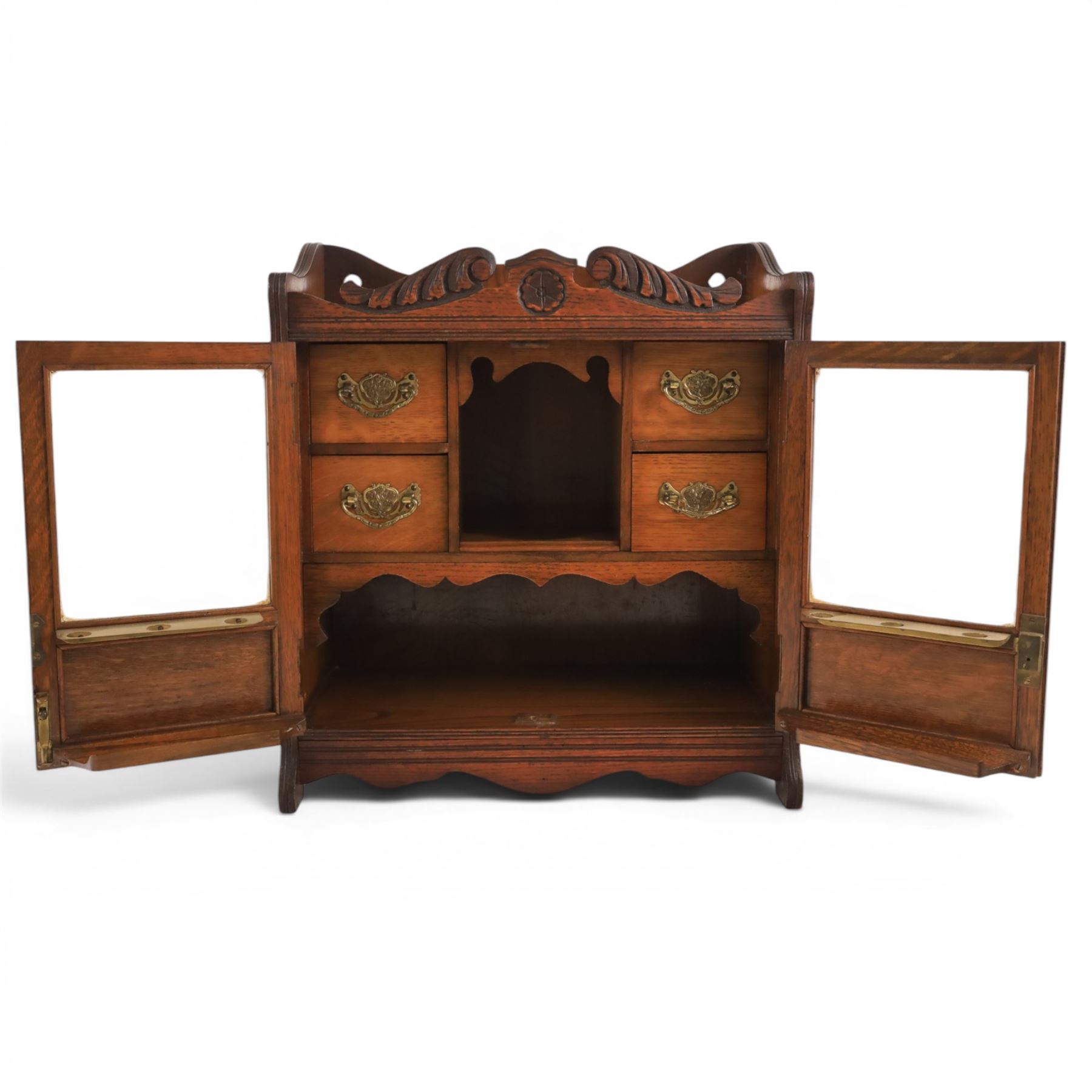 19th century oak table top smokers cabinet, with carved foliate pediment, the two beveled edge glass doors opening to reveal a fitted interior, with four drawers and fitted brass of pipe holders to each door, H46cm
