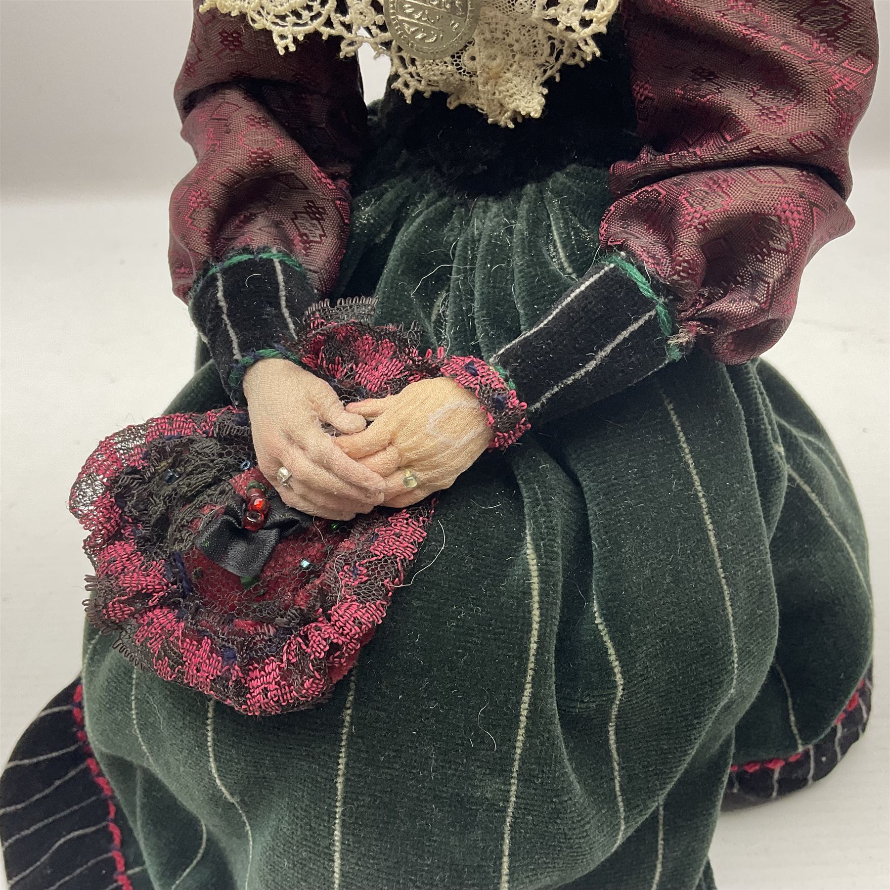 Anna Meszaros Hungary - hand made needlework finely detailed figurine of a pensive old lady seated on a stool wearing a lace trimmed long black and maroon dress and hat, clutching a lace bag H32cm Auctioneer's Note: Anna Meszaros came to England from her native Hungary in 1959 to marry an English businessman she met while demonstrating her art at the 1958 Brussels Exhibition. Shortly before she left for England she was awarded the title of Folk Artist Master by the Hungarian Government. Anna was a gifted painter of mainly portraits and sculptress before starting to make her figurines which are completely hand made and unique, each with a character and expression of its own. The hands, feet and face are sculptured by layering the material and pulling the features into place with needle and thread. She died in Hull in 1998.