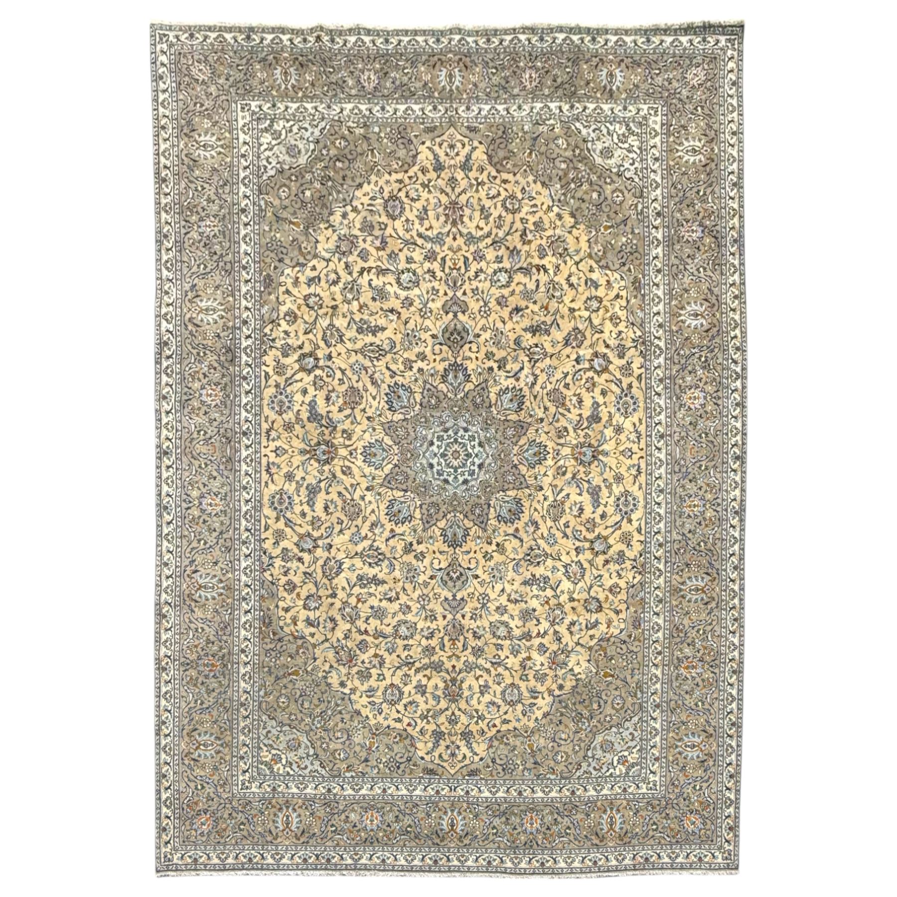 Central Persian Kashan pale khaki and ivory ground carpet, shaped central medallion enclosing small stylised motifs, the field decorated profusely with trailing foliate branches and plant motifs, guarded border with repeating floral design