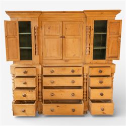 Large Victorian stripped pine reverse breakfront housekeeper’s cupboard, the moulded cornice above a central pair of panelled cupboard doors flanked by single cupboard doors and divided by turned baluster pilasters, the lower section fitted with an arrangement of twelve drawers with knob handles, raised upon bun feet