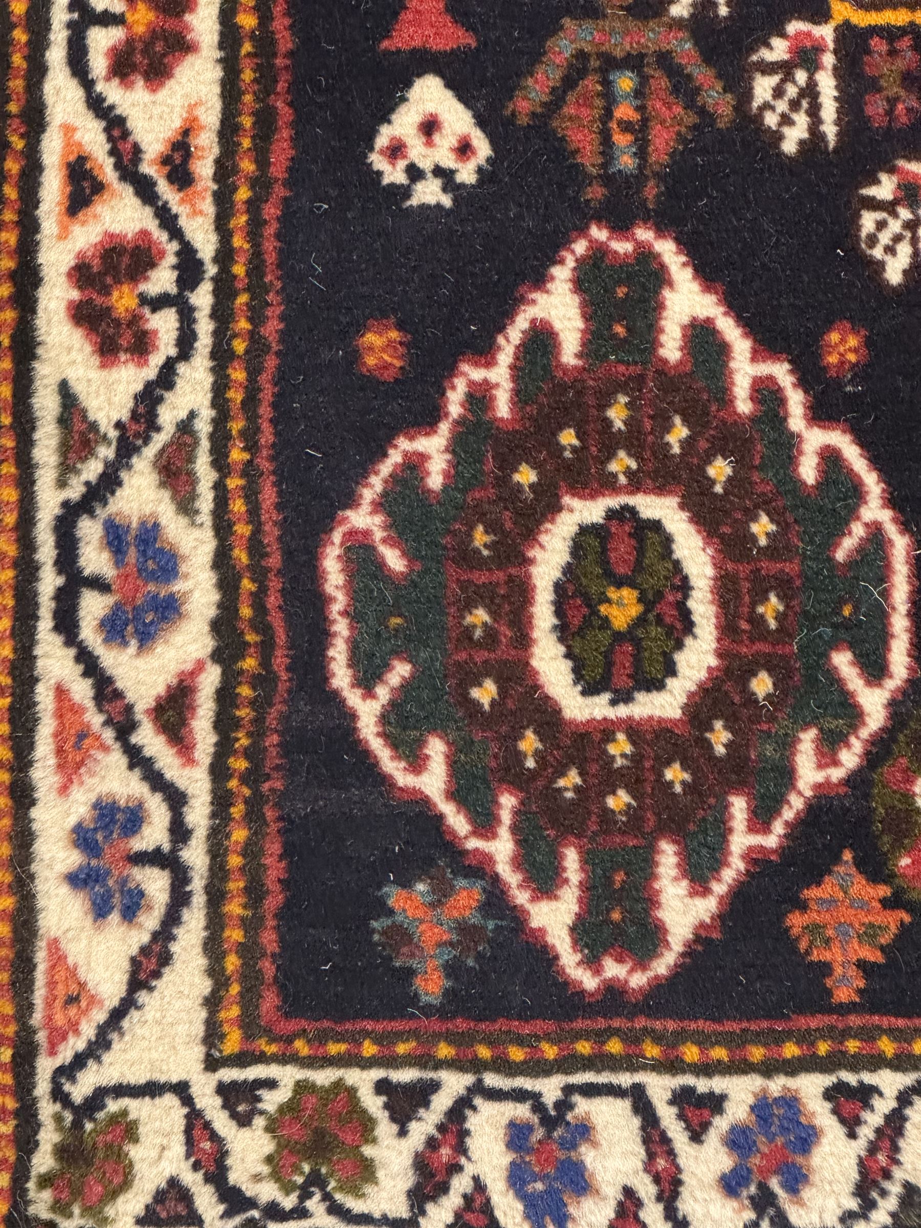 Persian Qashqai crimson ground runner, the field decorated with repeating diamond-shaped medallions flanked by angular floral motifs, the spandrels with intricate boteh designs, framed by an ivory border with stylised floral patterns and scrolling vines