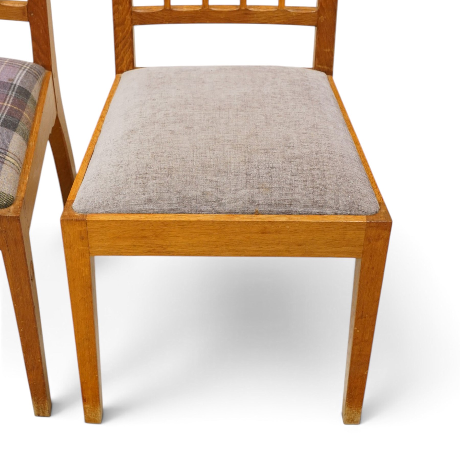 Acorn Industries - set of eight oak dining chairs, the shaped cresting rail over a fluted stick back, the drop-in seats upholstered in contrasting form with four pale mauve and four in purple tartan, raised on square supports, carved with acorn signature, by Alan Grainger, Brandsby