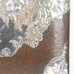 Edwardian silver mounted stationery box and silver mounted blotter, the box of rectangular form with curved front with applied repousse silver panels of putti within a scrolling foliate edge, the hinged cover opening to reveal an emerald green silk lined interior, the blotter with conforming silver mounted panels, each hallmarked William Comyns & Sons, London 1901, box H20cm W31cm D14cm, blotter H32cm W26.5cm