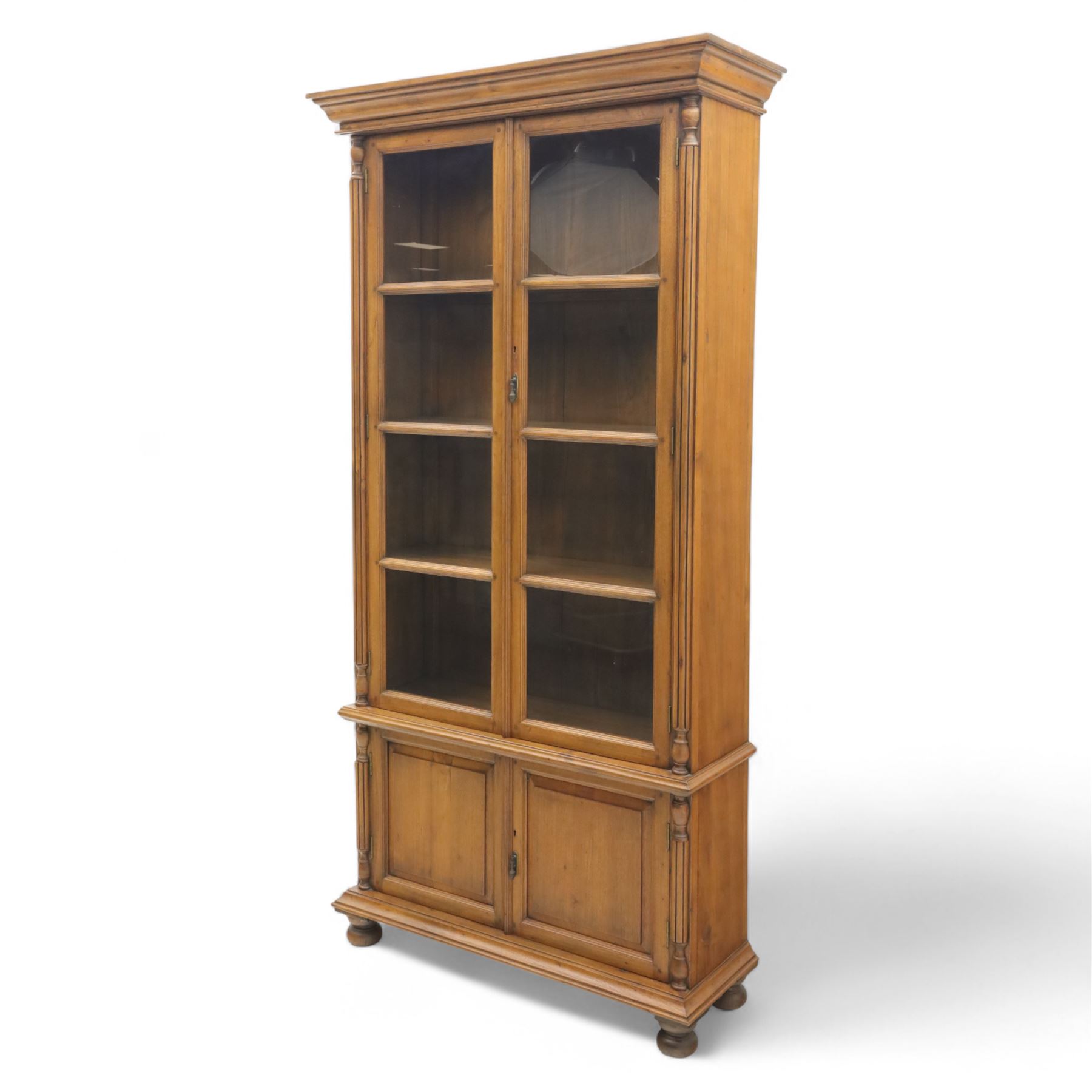 Pair of late 20th century Thai hardwood display cabinets, each with moulded cornice over twin glazed doors enclosing adjustable shelves, panelled cupboard doors below flanked by fluted columns, raised on bun feet