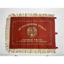 1970s Soviet banner printed in gold on a red ground, roughly translates as 'Transferable Banner - To the winner in the Socialist Competition' and 'Work Study Live by Communism' verso; wreath of wheat ears to either side; tassels on three sides 110 x 155cm