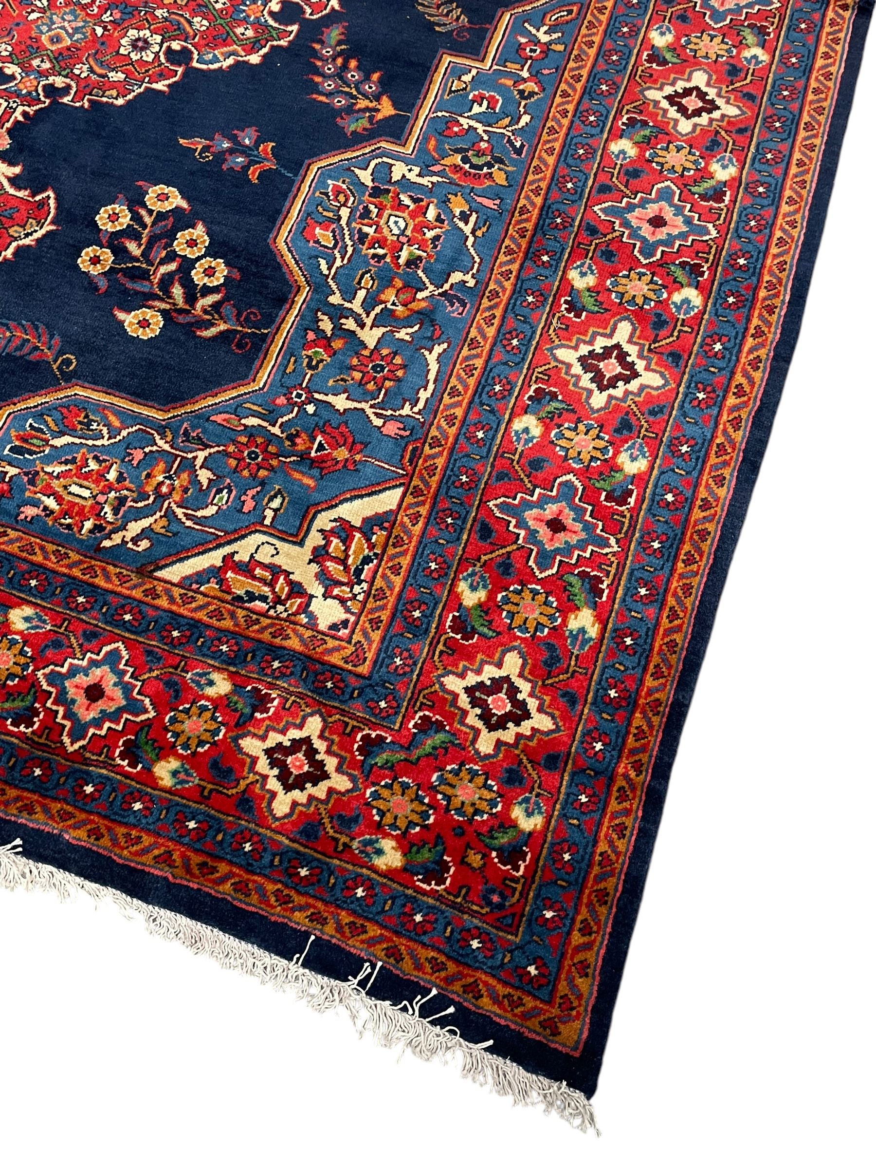 Persian Veis indigo ground carpet, the field with large pole medallion decorated with Herati motifs and surrounded by floral sprays, crimson ground border with repeating cross motifs and stylised flower heads, within guard stripes 
