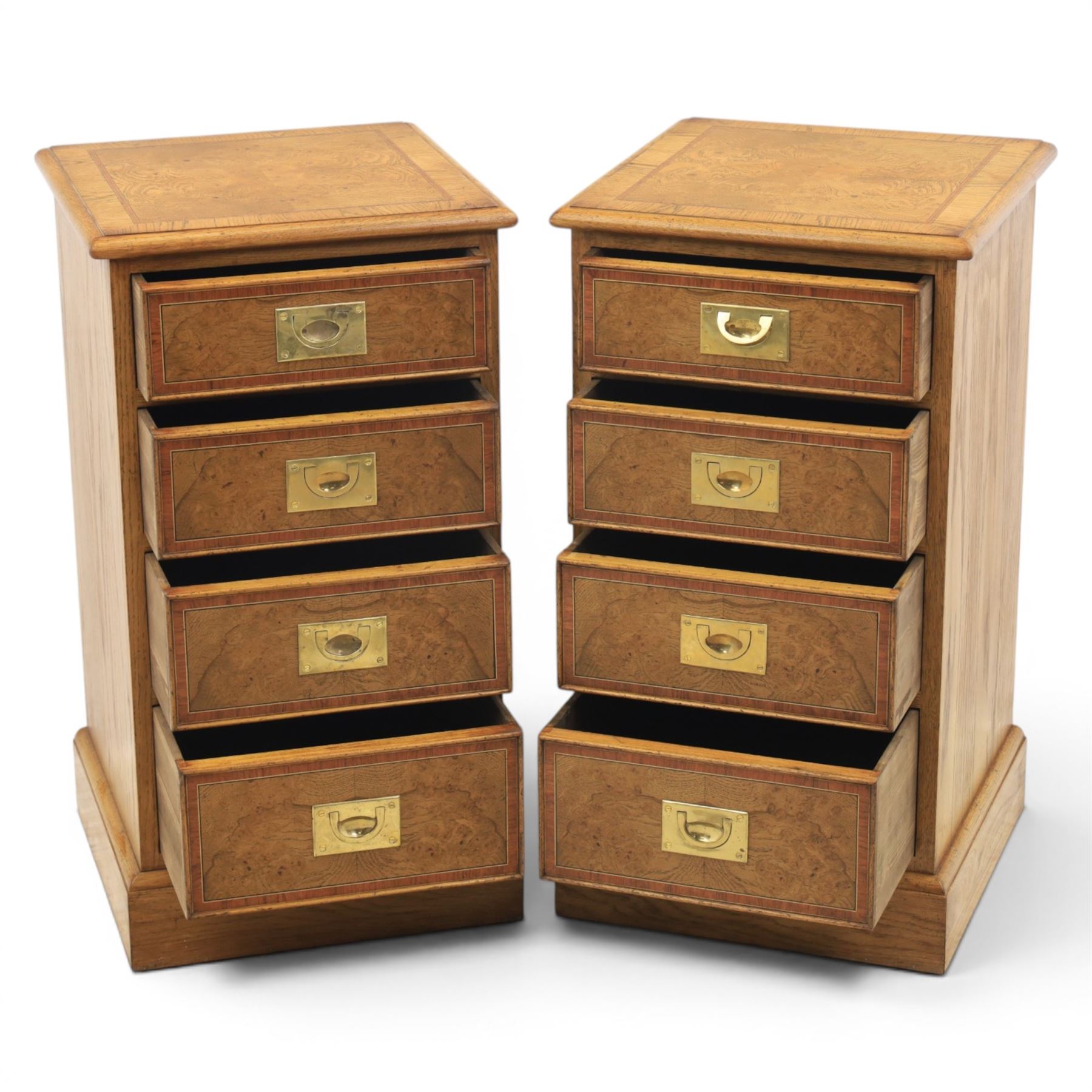 Pair of burr oak bedside tables with campaign brass handles, inlaid and crossbanded top, above four graduating drawers with cockbeaded edges, raised on a plinth base 