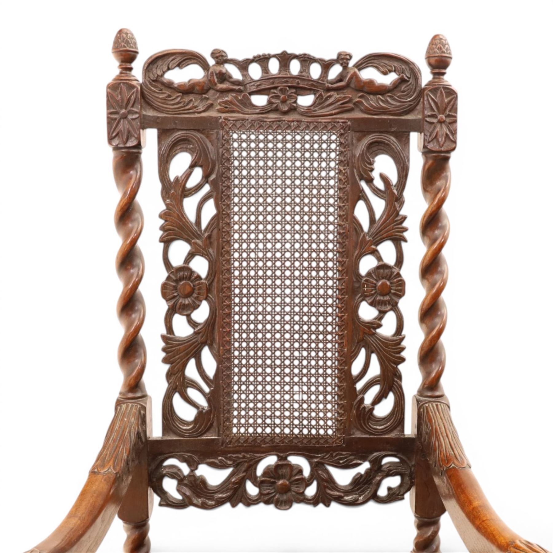 Late Victorian Jacobean Revival oak armchair, the caned back within a pierced and carved foliate frame surmounted by acorn finials, carved scroll arm supports, caned seat, on barley twist supports united by stretchers and carved front rail