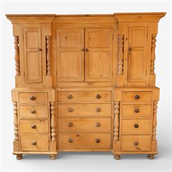 Large Victorian stripped pine reverse breakfront housekeeper’s cupboard, the moulded cornice above a central pair of panelled cupboard doors flanked by single cupboard doors and divided by turned baluster pilasters, the lower section fitted with an arrangement of twelve drawers with knob handles, raised upon bun feet