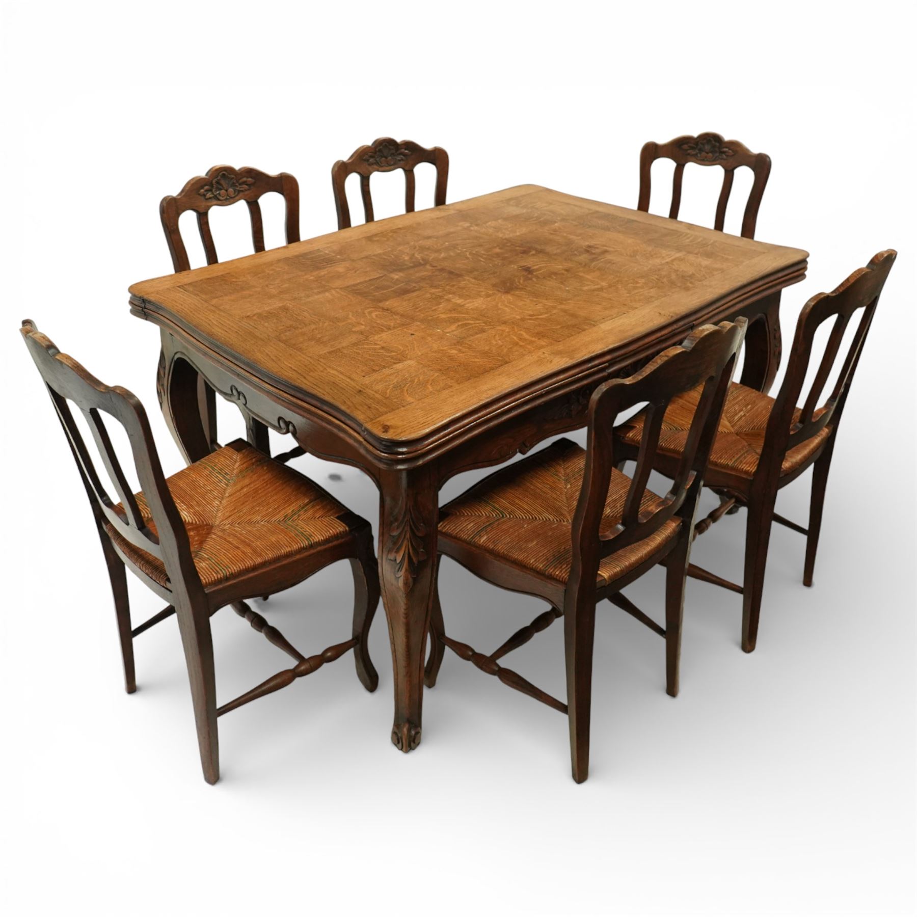 20th century French oak drawer-leaf extending dining table and six chairs, the rectangular parquetry top with moulded edge and rounded corners, pull-out draw leaves extending the table to 240cm, carved frieze with foliate detail, raised on cabriole supports with scroll terminals, the six matching chairs with shaped backs carved with floral motifs, paper cord seats woven with a green pattern, cabriole front supports and turned stretchers