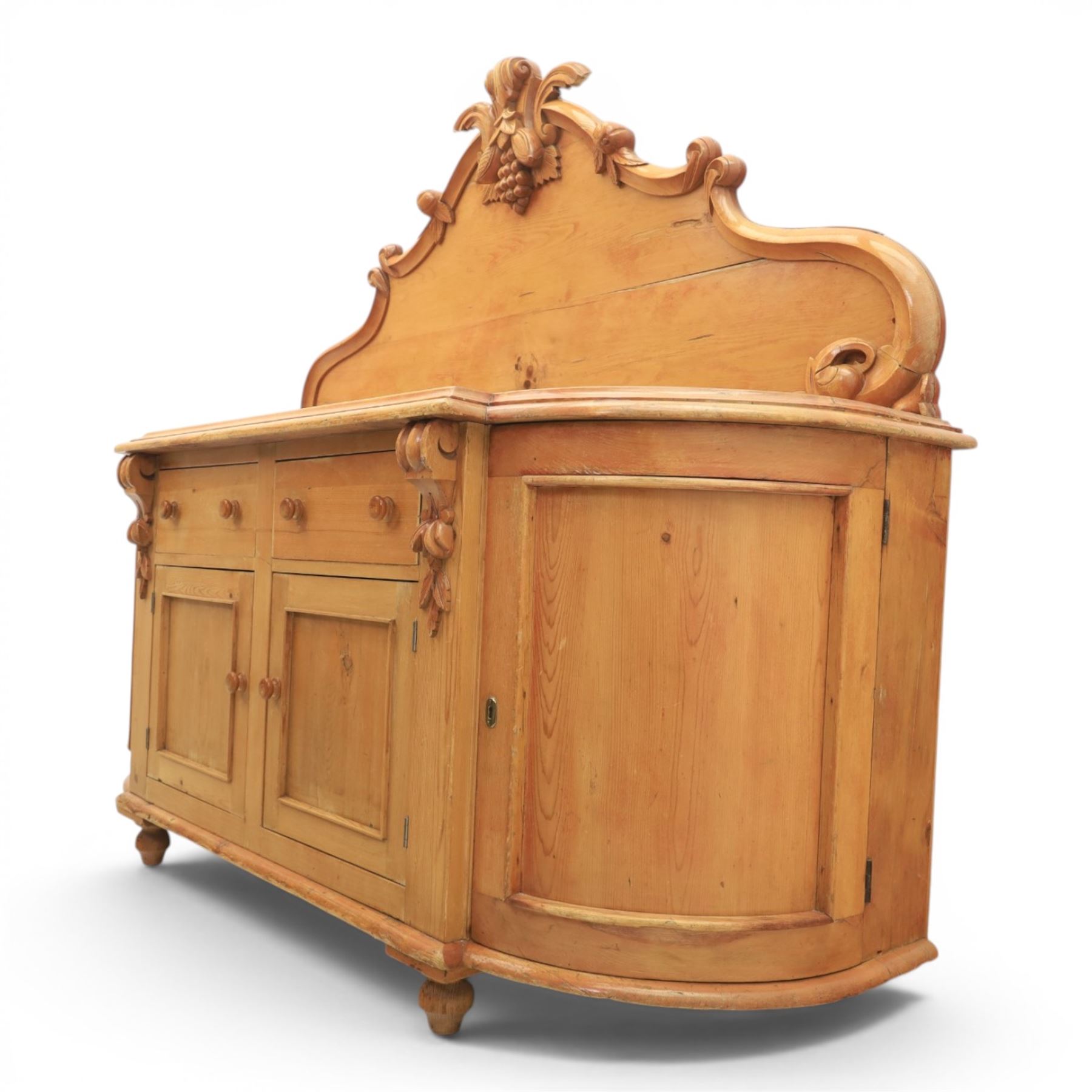 Victorian pine chiffonier, shaped moulded top with raised scroll carved back surmounted by carved fruit and foliate crest, fitted with two frieze drawers over two panelled cupboard doors, the outer cupboards of bowed form, carved foliate corbels, on plinth base