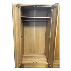 Contemporary light oak triple wardrobe, panelled doors with vertical linear design, left section enclosing hanging rail and single shelf, right section with adjustable shelves, over two drawers, on square stile supports