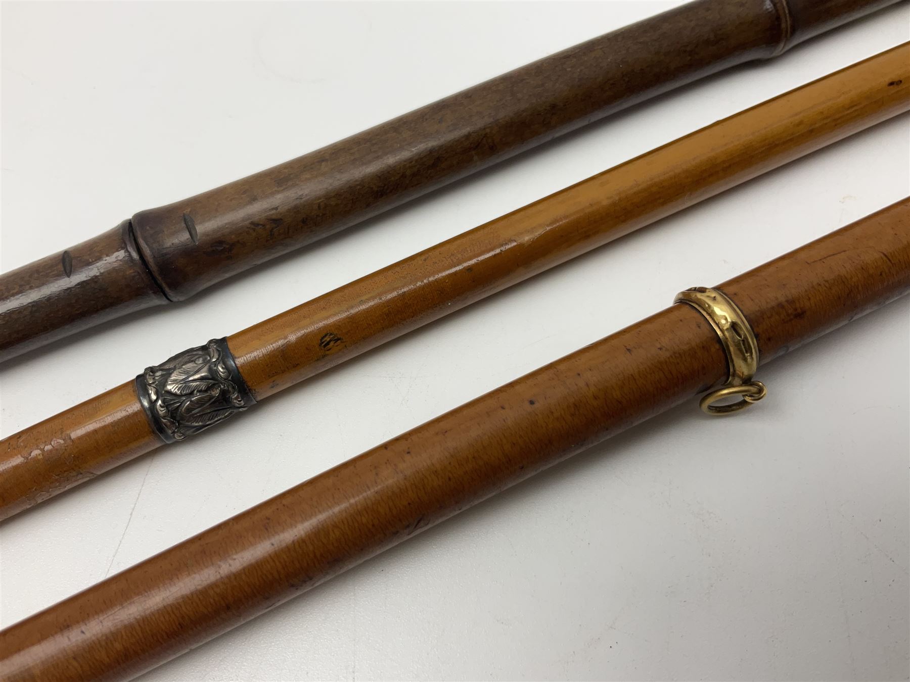 Early 20th century bamboo sword stick with 39cm oblong section blade L85cm overall; and two malacca cane swagger sticks, one with white metal mounts the other with yellow metal mounts (3)