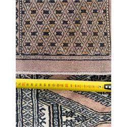 Large Persian Bokhara wool rug, the field decorated with repeating gul motifs in lozenge medallions across a dark ground, enclosed by multiple geometric borders in indigo, ivory and terracotta, from the region of Baluchistan