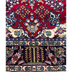 Central Persian Isfahan Carpet, hand-knotted, featuring a bold central rosette medallion on a rich red field, flanked by stylised floral sprays, scrolling foliage and mythical animals, within a broad indigo border decorated with alternating cartouches and flowerheads