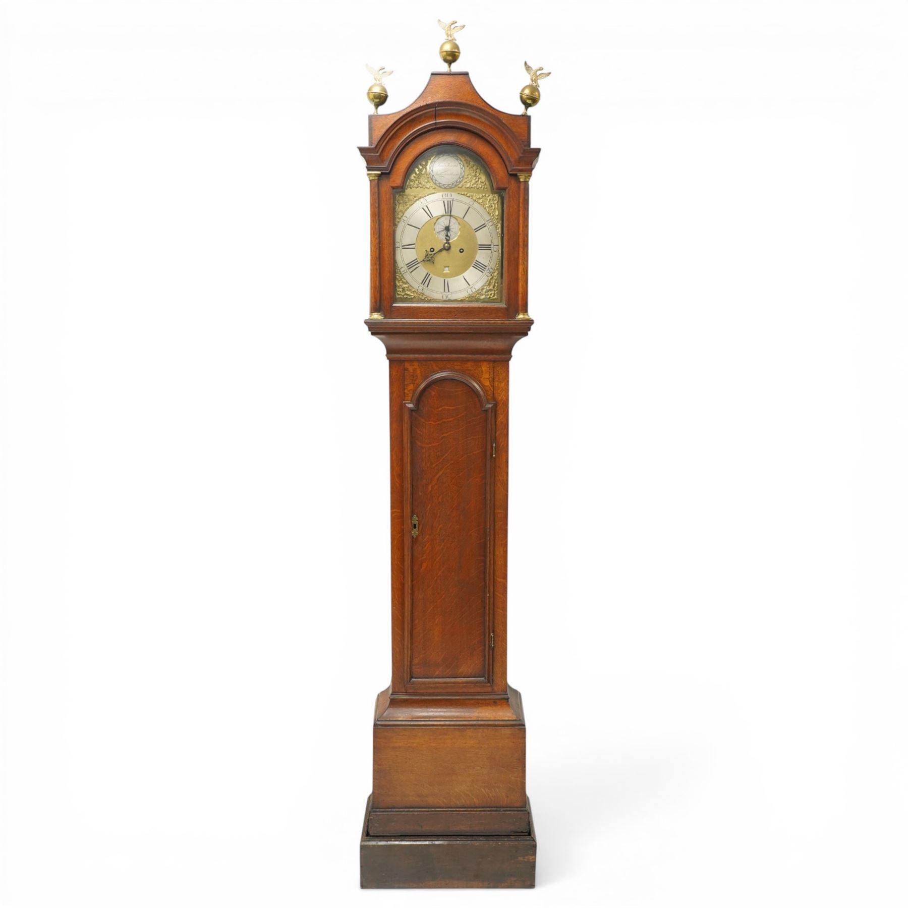 18th century oak eight-day longcase clock,  signed James Smyth, Saxmundham, the arched hood with brass ball and eagle finials, moulded arch pediment over turned columns, brass dial with silvered Roman chapter ring, Arabic minute track, matted centre with subsidiary seconds dial and calendar aperture, engraved boss to arch, the trunk with arched panel door, on stepped plinth base, with two weights and pendulum