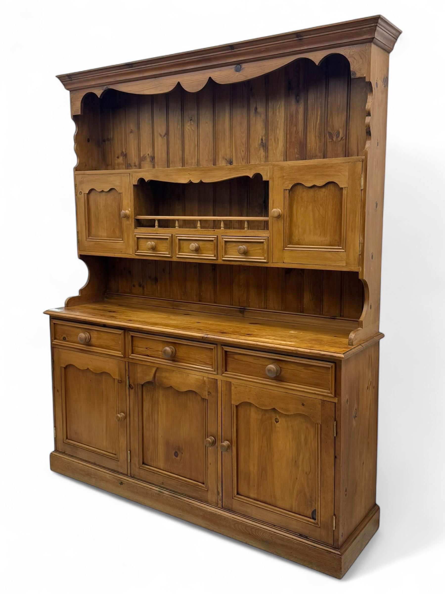 Traditional vintage pine kitchen dresser with scrolled cornice and rack with long shelf above a galleried shelf flanked by three short drawers and two cupboards, the base with three long drawers above three cupboards on plinth base  