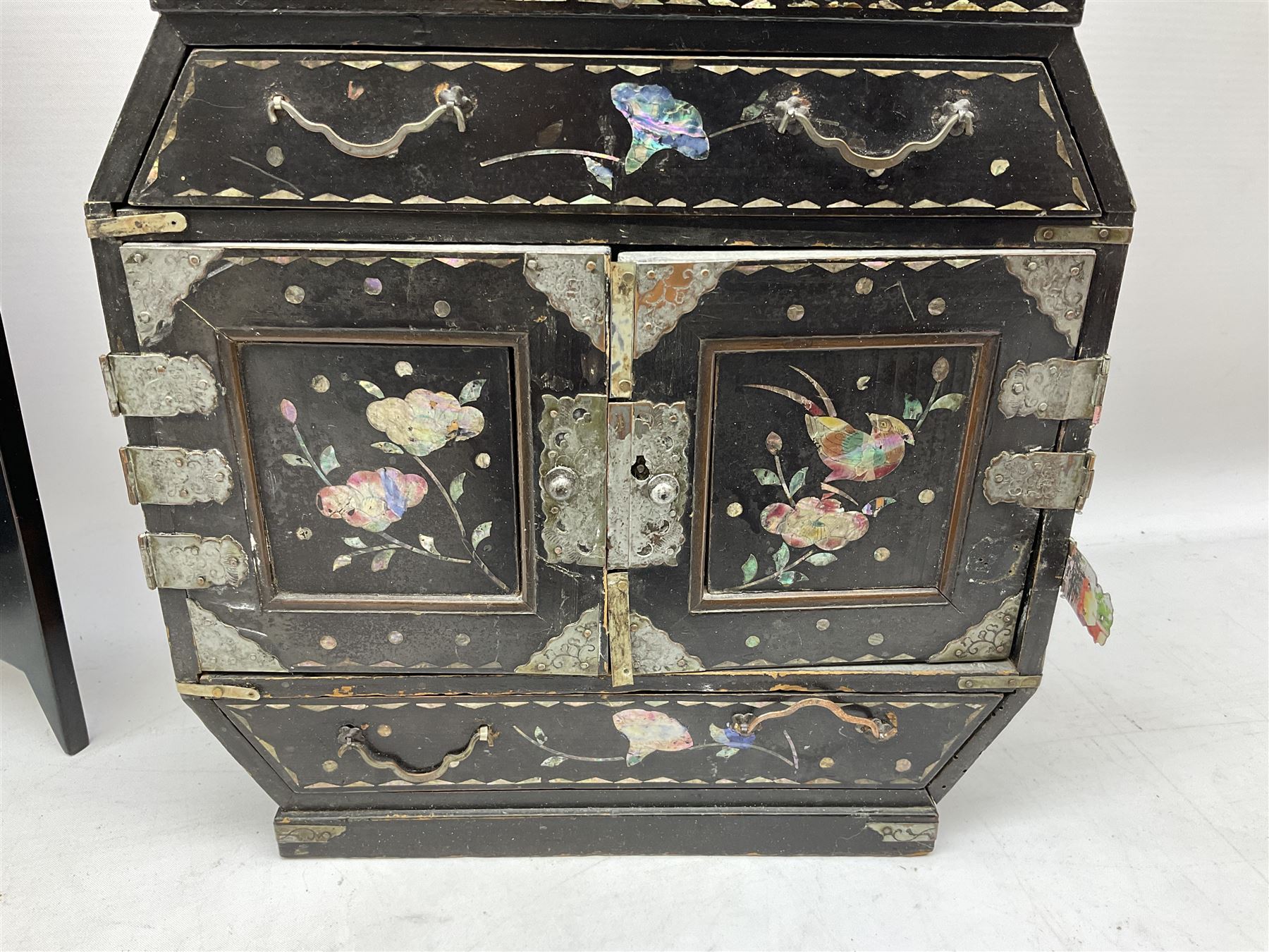  Late 19th / early 20th century Japanese lacquered table top cabinet, heavily decorated with mother of pearl inlay depicting blossoming branches, flowers and birds, the two hinged doors between longer drawers opening to reveal interior fitted with four short drawers, with lift up hinged canted lid, H28cm D9.5cm W23cm, together with mother of pearl inlaid miniature folding screen, dish decorated with walking figures with crimped edge, boxes decorated with flowers, birds and gilt etc