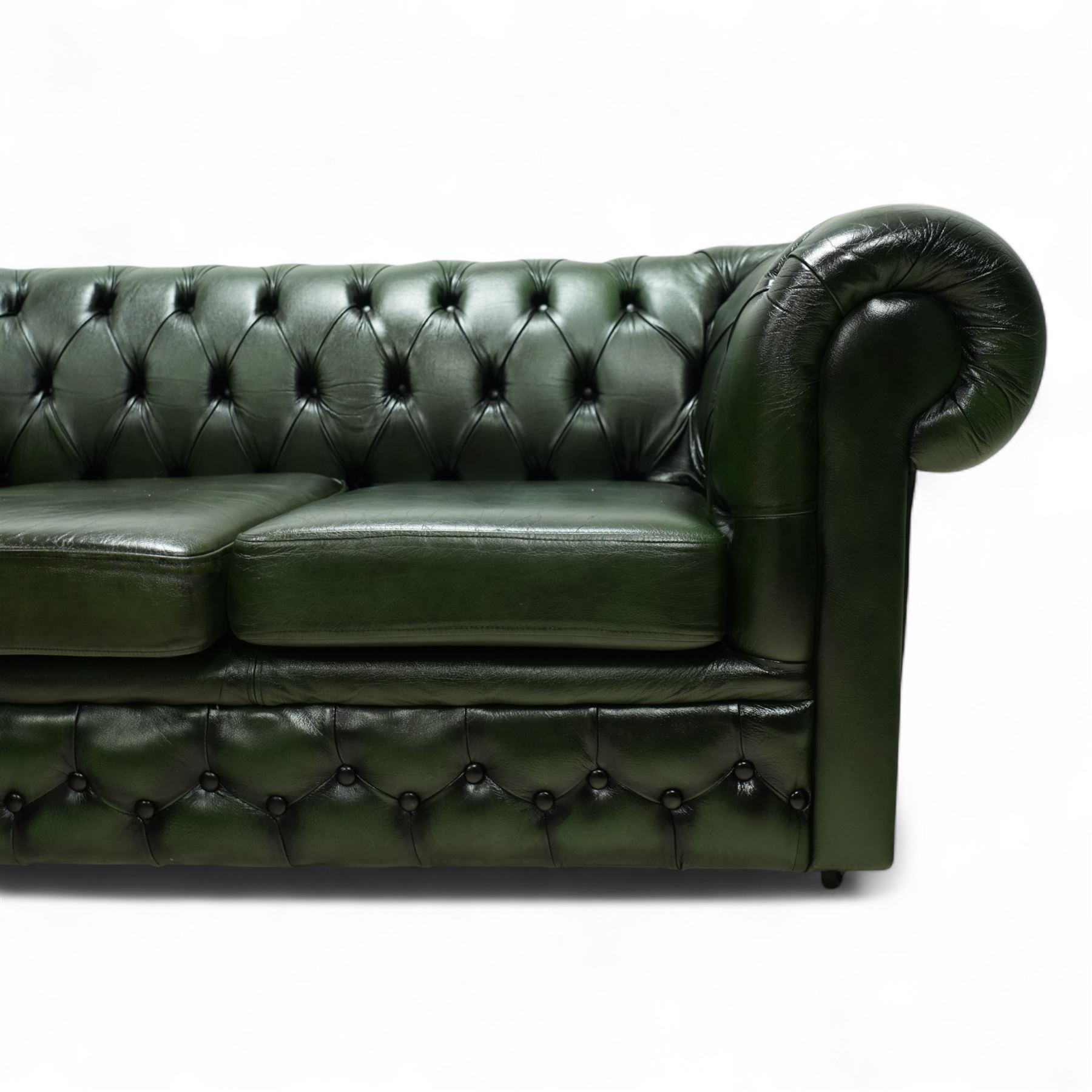 Late 20th century chesterfield style sofa upholstered in green leather, with deep buttoned back and arms above three loose cushions, continuous scroll arms and front, on concealed block feet