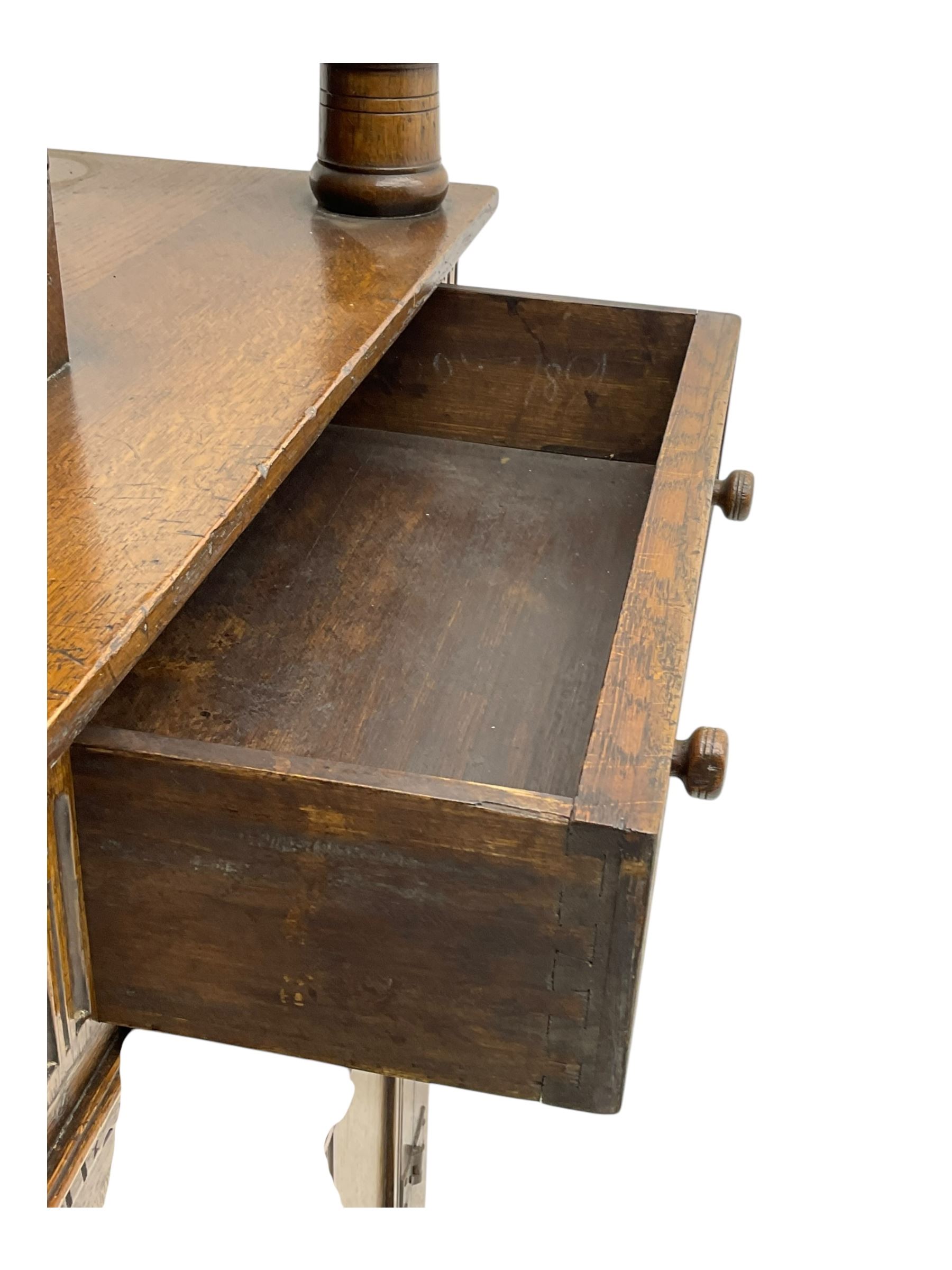 Jacobean design oak court cupboard, upper section with carved arched panelled cupboard door flanked by turned columns, beneath carved and moulded frieze, lower section fitted with two drawers over two cupboard doors with gothic arched panel decoration, raised on stile supports