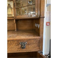 Shapland and Petter - Arts & Crafts period oak dresser, raised gallery top with spade balustrade, central bevelled mirror flanked by two cabinet, astragal glazed doors with yellow tinted glass and bullseye panes, the sides with pierced heart shaped decoration, fitted with two drawers and two double cupboards, enclosed by linenfold panelled doors,  copper work strap hinges and fixtures, on shaped spade feet, the locks stamped 'S&P'