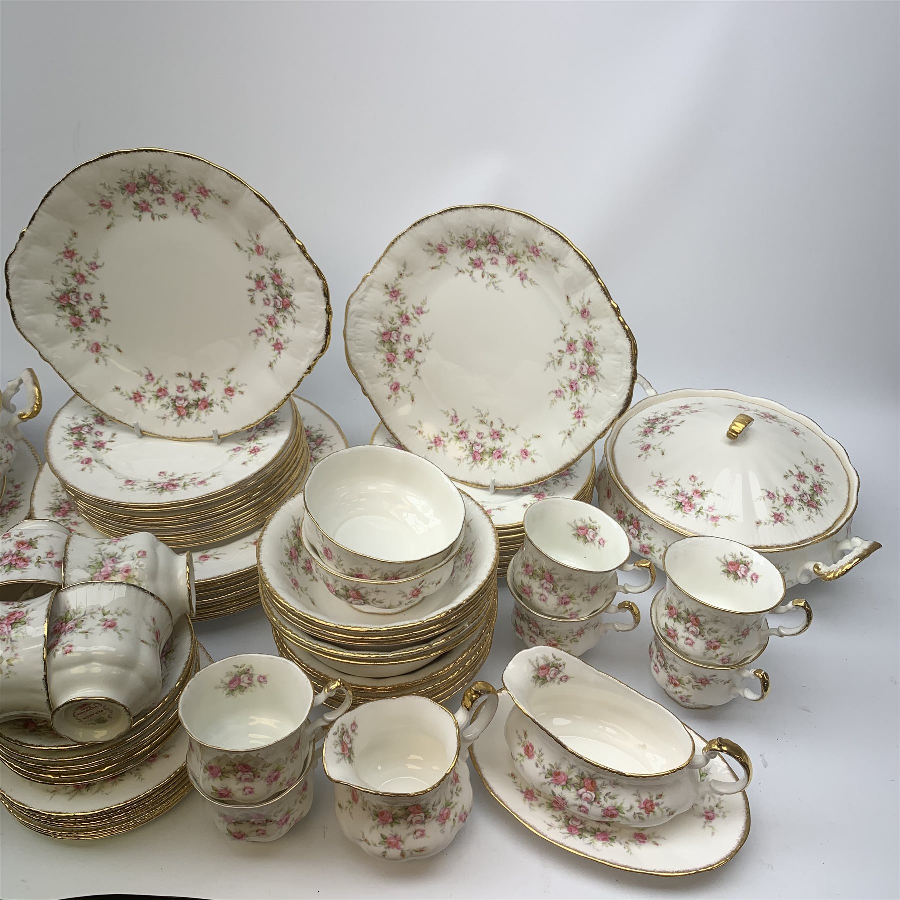 Paragon Victoriana Rose pattern tea and dinnerware, comprising fourteen teacups, sixteen saucers, fourteen side plates, two milk jugs, two open sucriers, two sandwich plates, a cake stand (lacking central support), two tureen and covers, eight dinner plates, twenty one dessert plates, eleven bowls, and sauce boat and stand. 