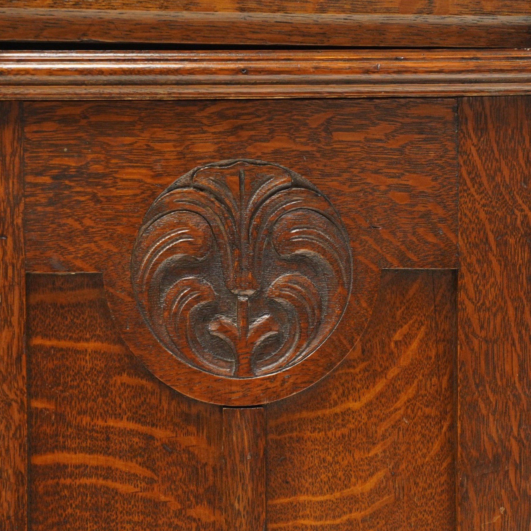 Arts and Crafts oak dresser, projecting moulded cornice above three glazed panels with coloured leaded glass floral panels, flanked by two glazed doors enclosing two adjustable shelves, open mirrored recess below with mirrored back, the base fitted with two short drawers over two central drawers flanked by carved panelled cupboard doors, ornate brass handles, raised on tapering square legs