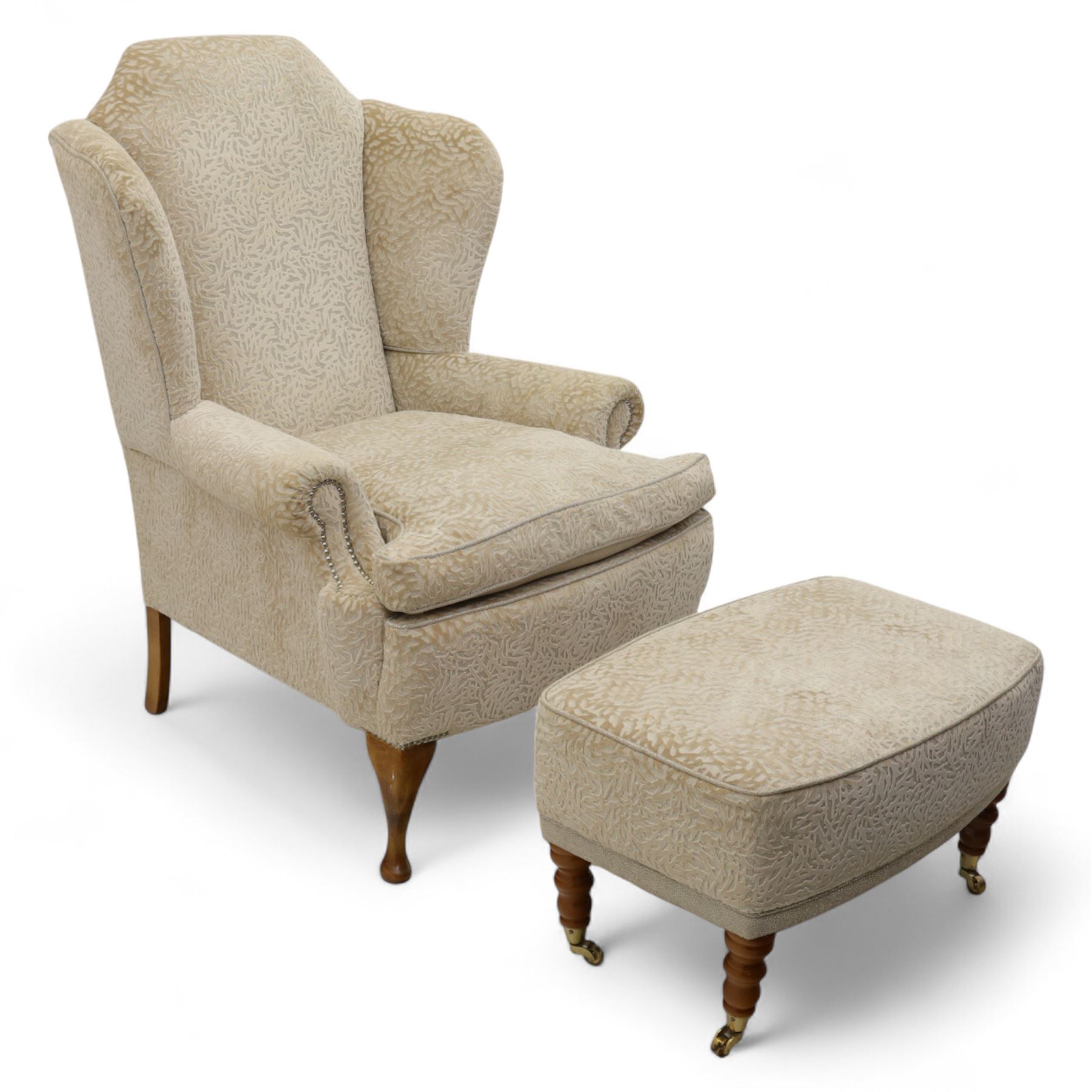 Late 20th century wingback armchair and matching footstool, upholstered in beige embossed fabric with brass stud edging, on cabriole legs and splayed rear legs, together with a matching footstool on turned supports terminating in brass castors (Stool H 42cm, W 75cm, D 47cm)
