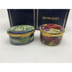Two Moorcroft enamel boxes, the first example of oval form, decorated with lily of the valley upon a blue ground, the second of circular form, decorated in pomegranate pattern, each with fitted box  