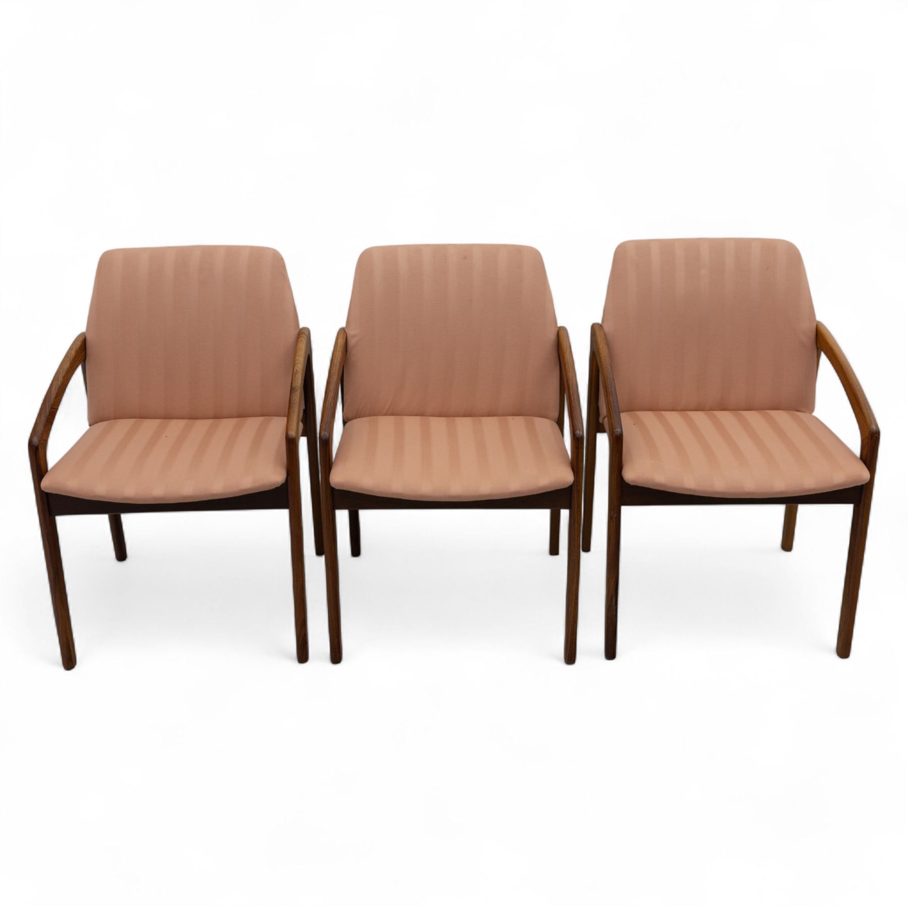 Mid-20th century Danish teak armchairs, each with curved open arms and upholstered seat and backrest in salmon pink striped fabric, raised on tapering legs