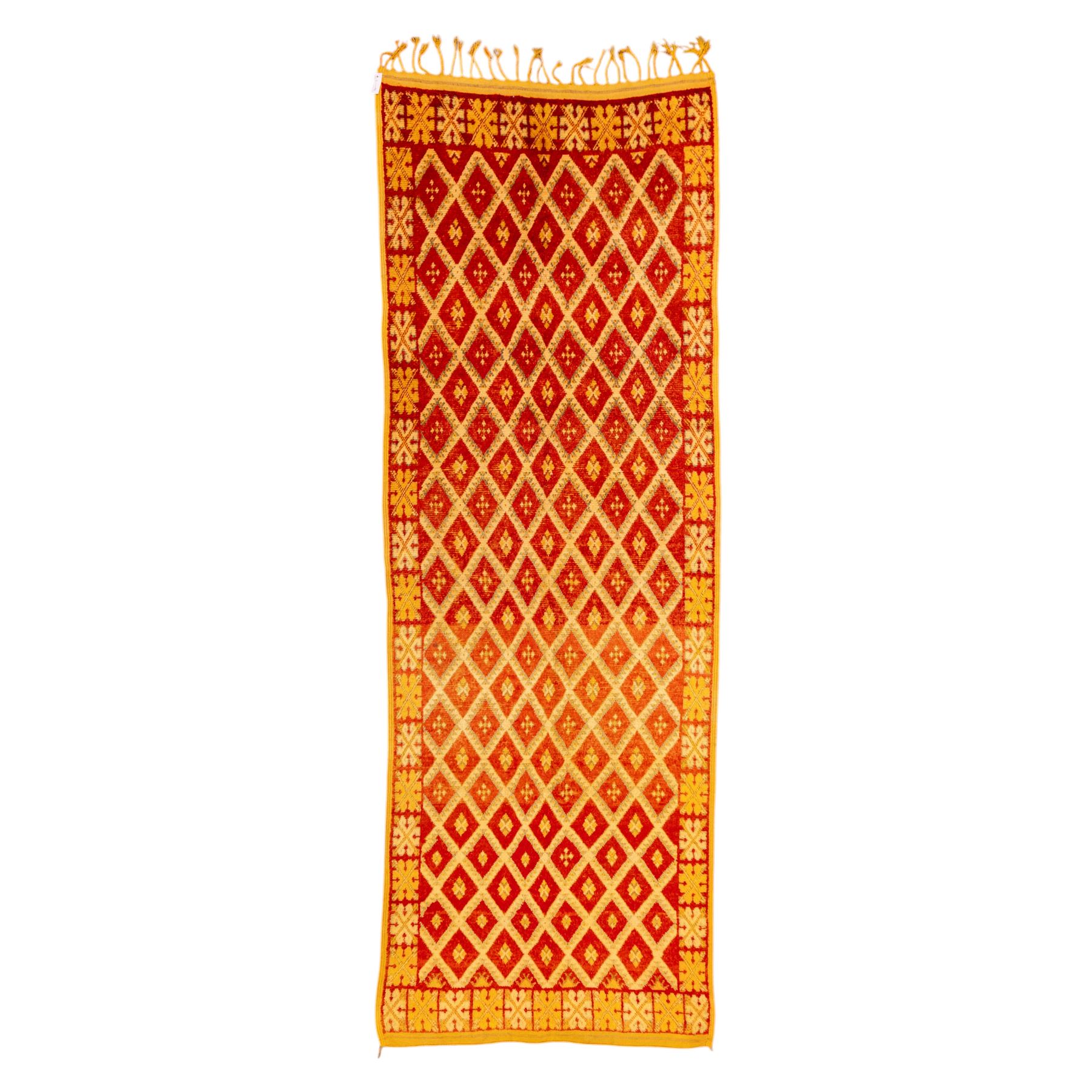 Moroccan Berber hand knotted runner, the red and orange ground woven with an all over lattice of lozenge motifs enclosing small geometric devices, within narrow patterned borders, finished with fringe to one end