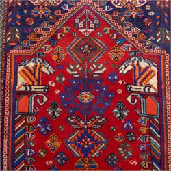South West Persian Qashqai hand-knotted runner, madder red field  with central vertical succession of stepped lozenge medallions enclosing angular tribal devices and stylized floral motifs, principal medallion in deep indigo with ivory and sky blue highlights, field densely scattered with small geometric ornaments, hooked elements and zoomorphic forms, triangular indigo spandrels enclosed within multiple narrow guard stripes and principal border, with cotton fringe ends 