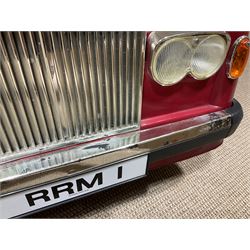 Early 1980s Rolls-Royce Corniche 'pedal' car by Sharna Tri-ang Limited, registration no.RRM1, steel chassis with treadle pedals, red moulded plastic body with flexible plastic 'Spirit of Ecstasy' car mascot on the radiator cap, opening boot lid, dashboard with decals of faux wood panelling and gauges, battery powered working electric lights, Sharna 235/70HR15 wheels with Rolls Royce hub caps, L123cm; together with two keys on RR fob, instructions manual in wallet, date stamped 17 November 1983, toy road tax disc dated 31.01.83/84 and original battery charger. 
Auctioneers Note: In 1983 Sharna Tri-ang Ltd., based at Lumb Mill in Droylsden, Manchester, took over from Tri-ang Toys at Merthyr Tydfil. They went on to launch a new range of toys based on children's TV programs, such as Knight Rider, Street Hawk, Roland Rat, The A-Team, The Get A-Long Gang and Postman Pat, as well as Rolls-Royce Corniche pedal cars, which were available in red, white or blue. 