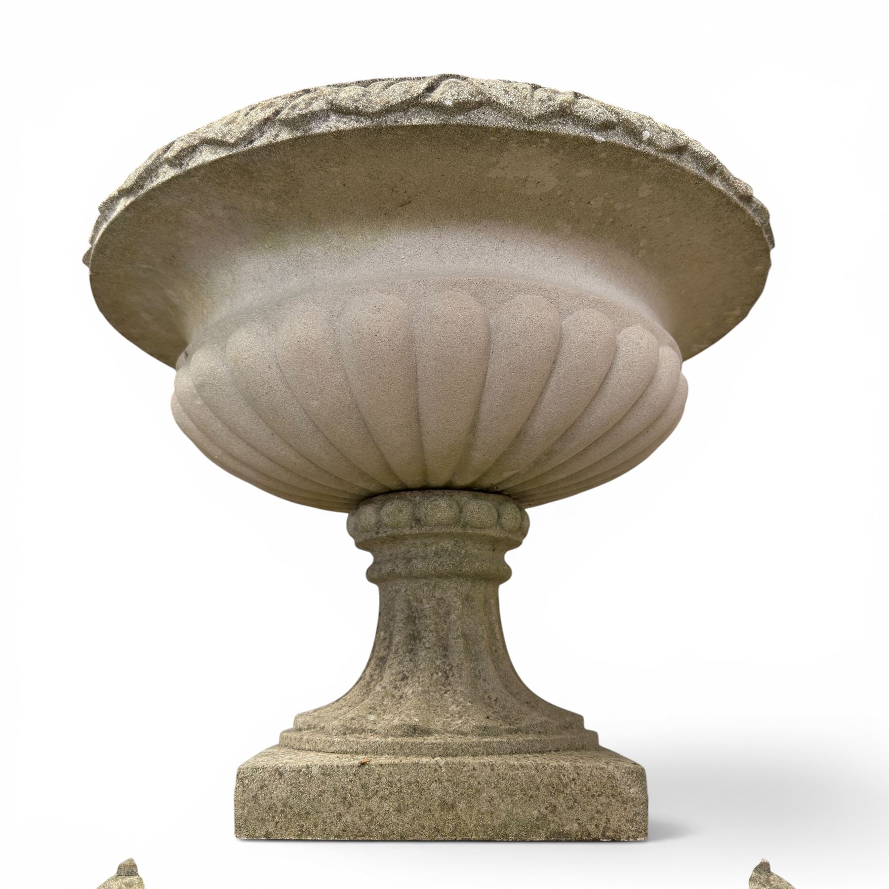 Pair of weathered cast stone Neoclassical design garden Kylix shape urns, foliate moulded rim over a gadrooned underbelly, the scalloped socle over a rectangular pedestal with faux-panelled sides, stamped with stylised ‘H’ monogram