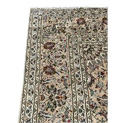 Persian Kashan ivory ground carpet, central rosette medallion with projecting palmettes, densely decorated field depicting trailing leafy branches and stylised plant motifs, the border with similar scrolling pattern, within floral pattern guard stripes 