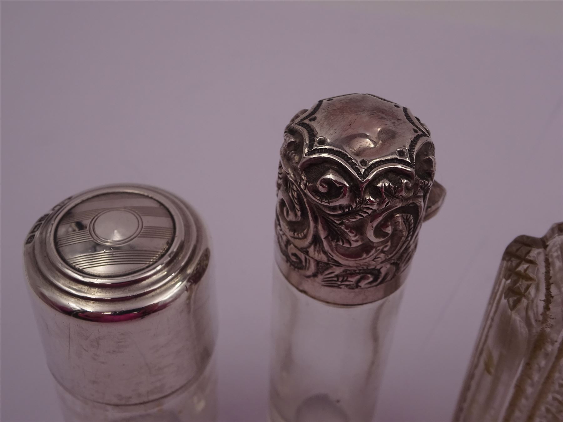 Four silver mounted glass scent bottles, including a Victorian cut glass example with embossed silver cover, and three cylindrical plain glass examples, on with engine turned decoration, three with glass stoppers, together with a pair of silver salts and spoons, all hallmarked, tallest H8cm