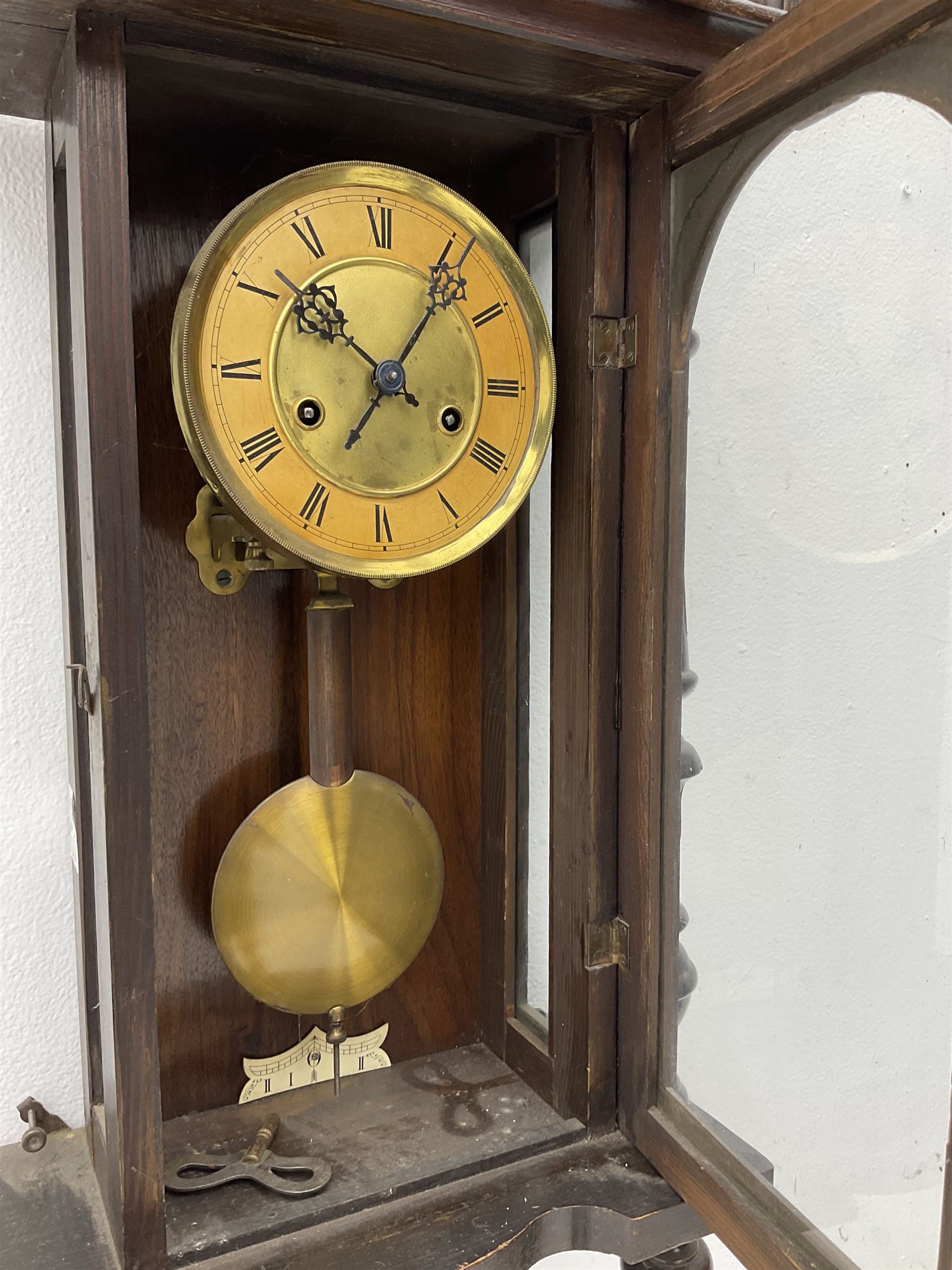 A late 19th century German wall clock c1880 with an 8-day HAC spring driven movement striking the hours on a coiled gong, in a mahogany case with a tall pediment and deeply turned columns flanking a full-length glazed door, with a two-part dial with a gilt centre and ivorine chapter, with Roman numerals, minute track and pierced gothic designed hands, spun brass faced pendulum and beat plate. With Key.



