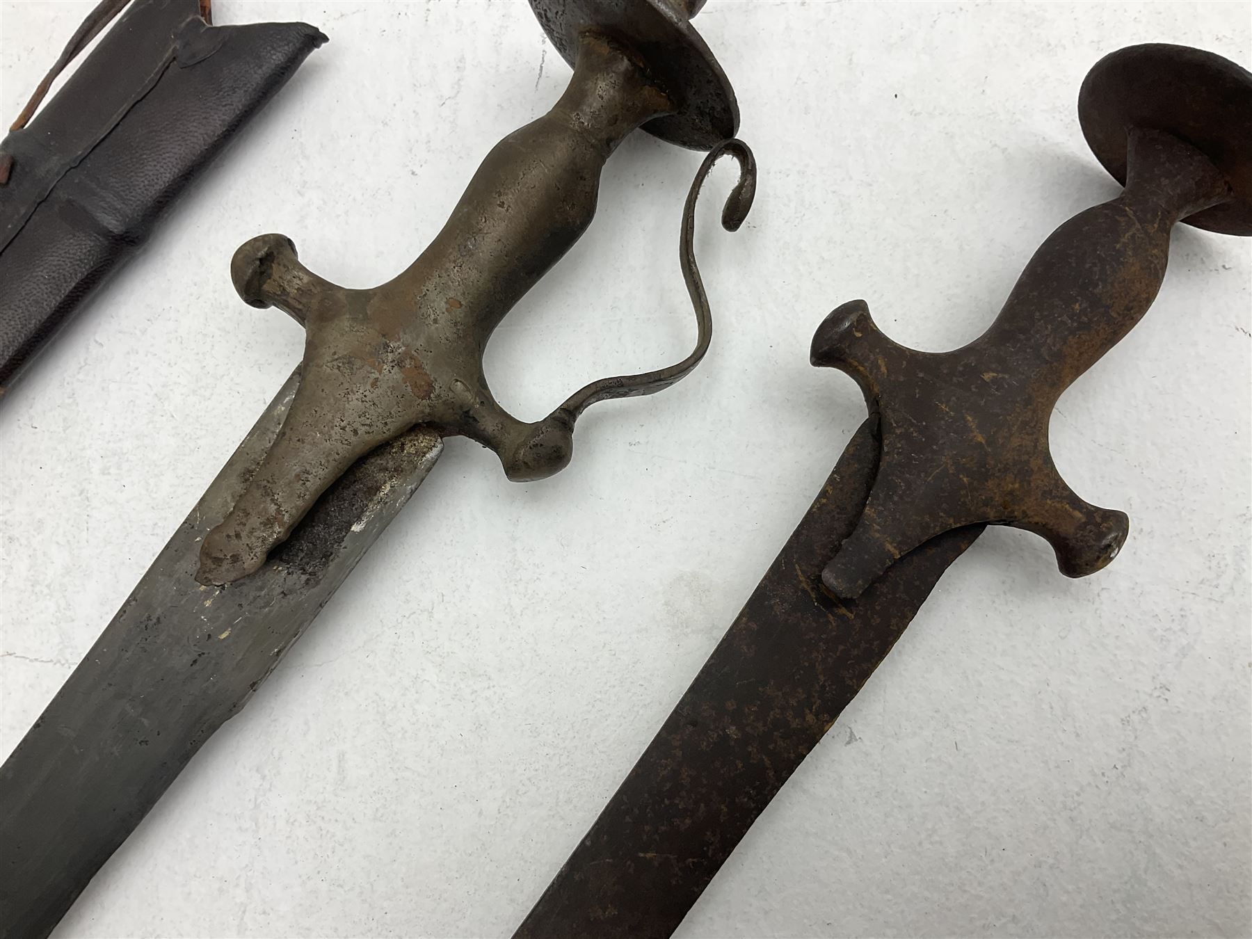 Late 19th/early 20th century Indian Tulwar sword with 81cm plain curving steel blade and iron hilt with extended langets, knucklebow and spiked pommel; in leather covered scabbard L100cm overall; and another Tulwar lacking scabbard in almost relic condition (2)