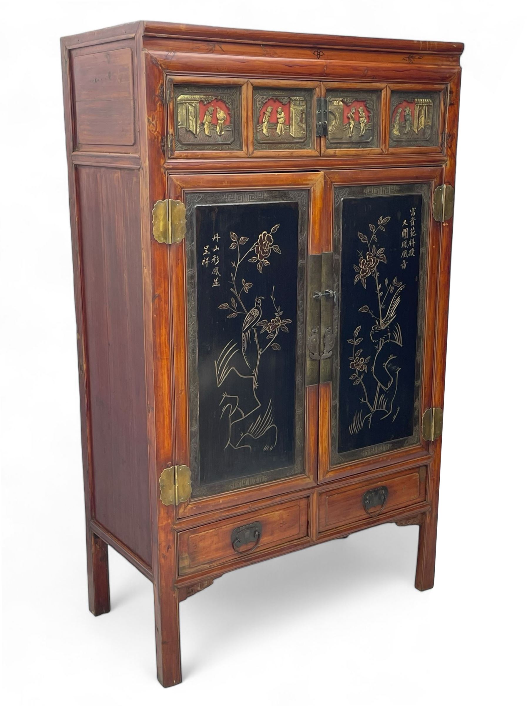 Late 19th century Chinese Qing dynasty red and black lacquered wood cabinet,  Fujianese province, upper cupboard enclosed by two doors with relief carved and gilt panels depicting figures behind glass, the large cupboard enclosed by two panelled doors carved with trailing foliate branches and birds, inscribed with Chinese characters, to the left ‘The red mountains are in the shape of Phoenixes and appear auspicious’ and to the right, ‘Wealth and honour are given by flowers and I hear the sound of the phoenix', fitted with two drawers, on square supports with carved brackets 