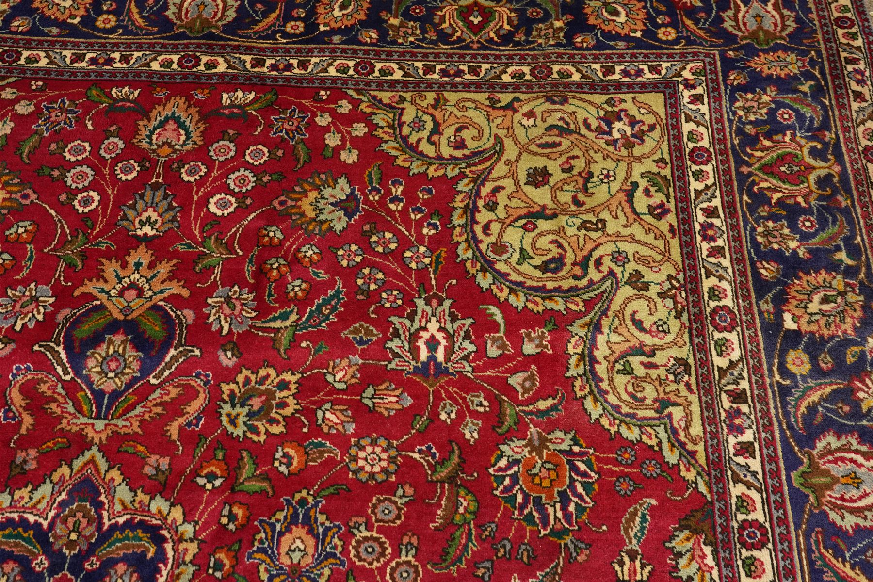 North East Persian Meshad hand-knotted carpet, crimson field with central lobed medallion in tones of indigo, ivory and soft blue, with an all-over arrangement of scrolling vinery, palmettes, and floral  sprays, conforming spandrels, main border of stylized floral vinery framed by multiple guard borders, with cotton fringe ends